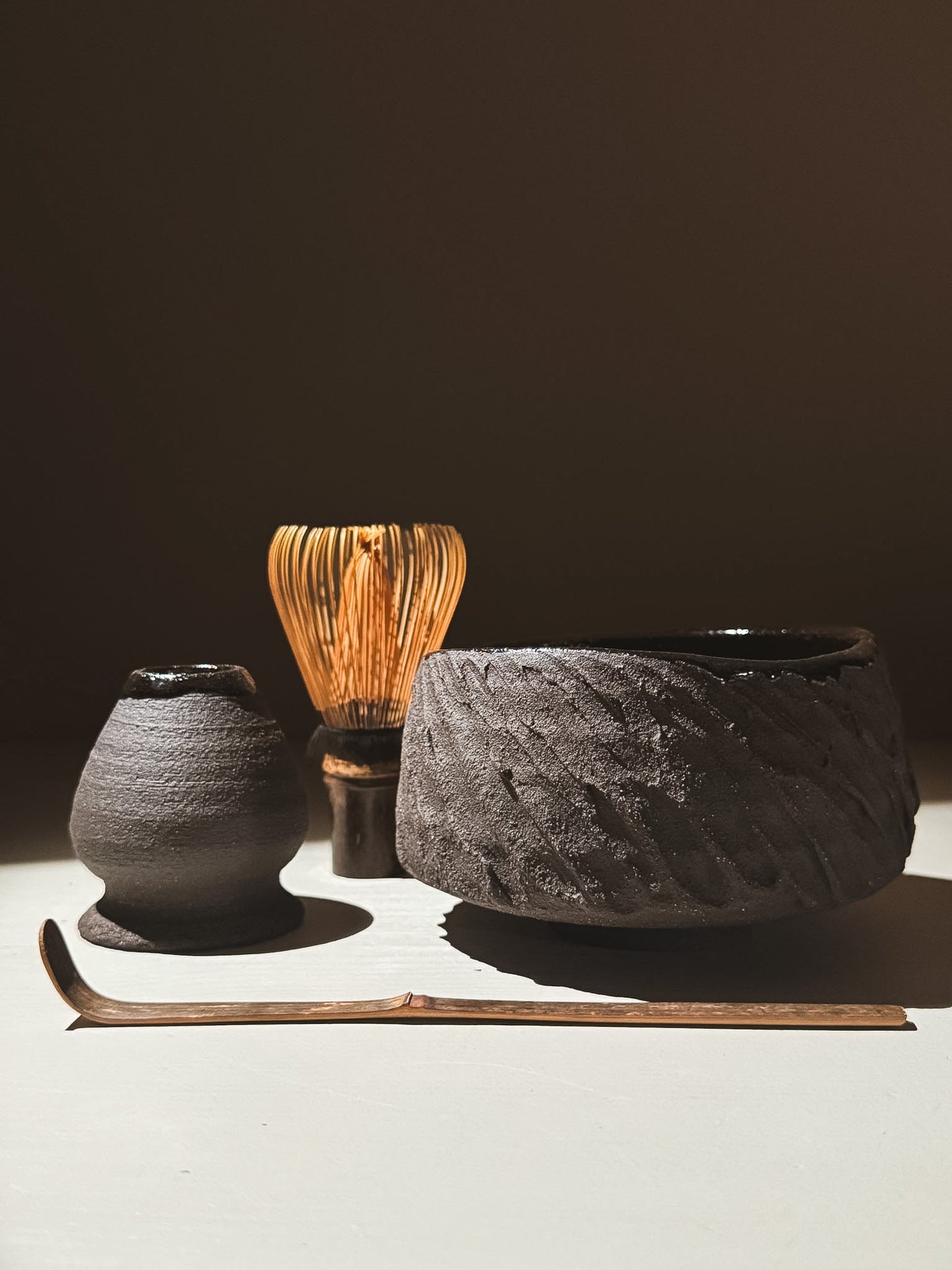 Kuro Matcha Bowl #08 displayed next to a bamboo whisk, a small black vessel, and a slender tea scoop on a neutral background.