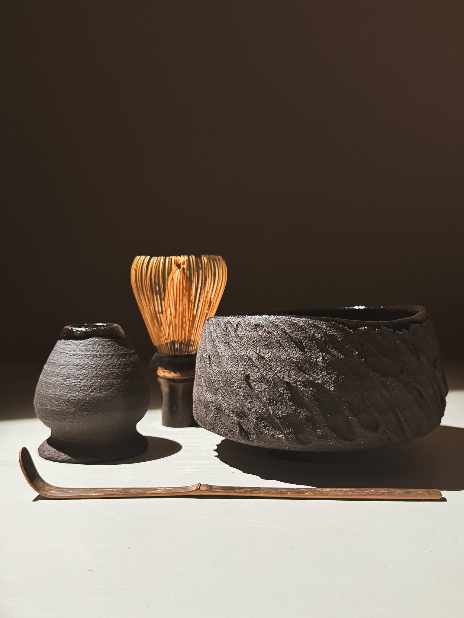 Kuro Matcha Bowl #08 displayed next to a bamboo whisk, a small black vessel, and a slender tea scoop on a neutral background.