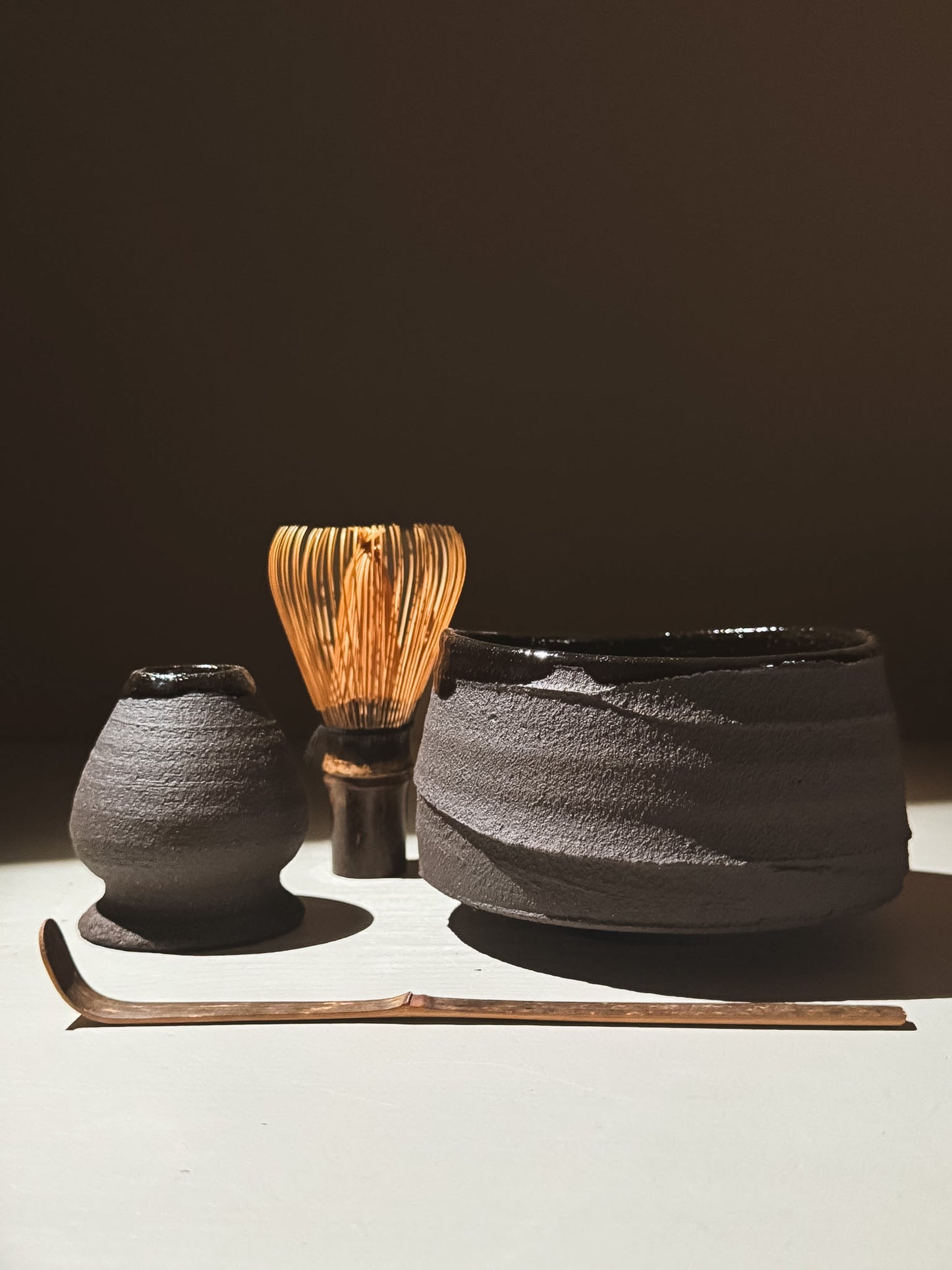 Kuro Matcha Bowl #10 with matcha whisk and scoop, showcasing earthy textures and dark tones.