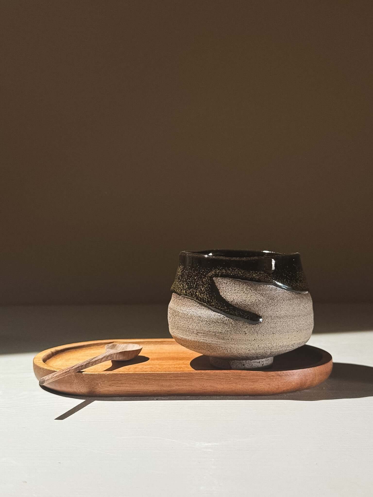 Yunomi Cup - Kuro Ash #02 on a wooden tray, showcasing its grey stoneware and glossy black glaze with natural movement.
