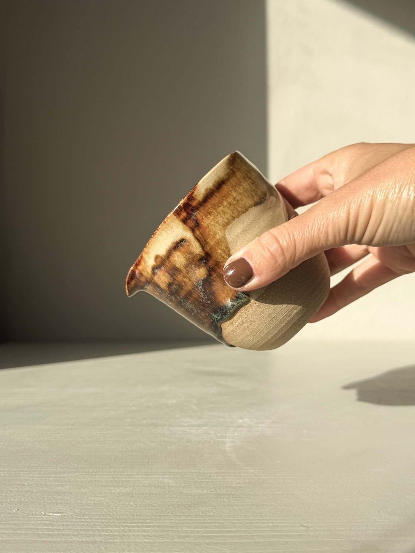 Hand holding Pouring Jug – Inyo Series #02, showcasing handmade ceramic with glossy tenmoku and clear glaze on toffee clay.