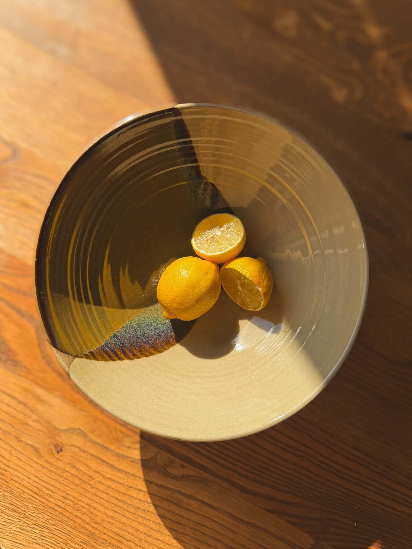 Large Bowl - Inyo #01 with lemons, featuring Tenmoku and clear glaze, showcasing organic shape and subtle rim curves on wood surface.