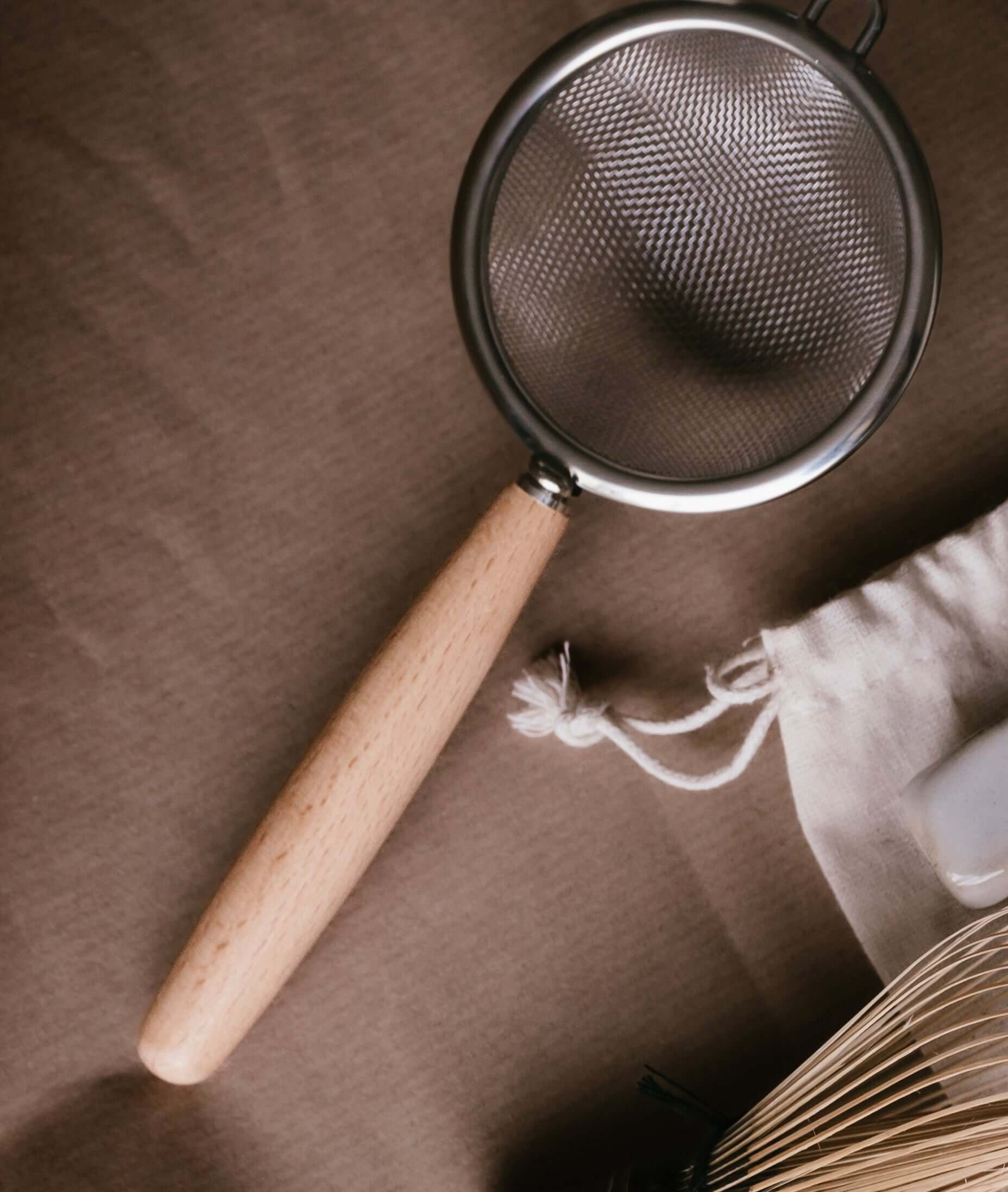 Stainless steel Tea Strainer with wooden handle, perfect for sifting matcha or loose leaf tea, shown with handmade ceramic accessories.