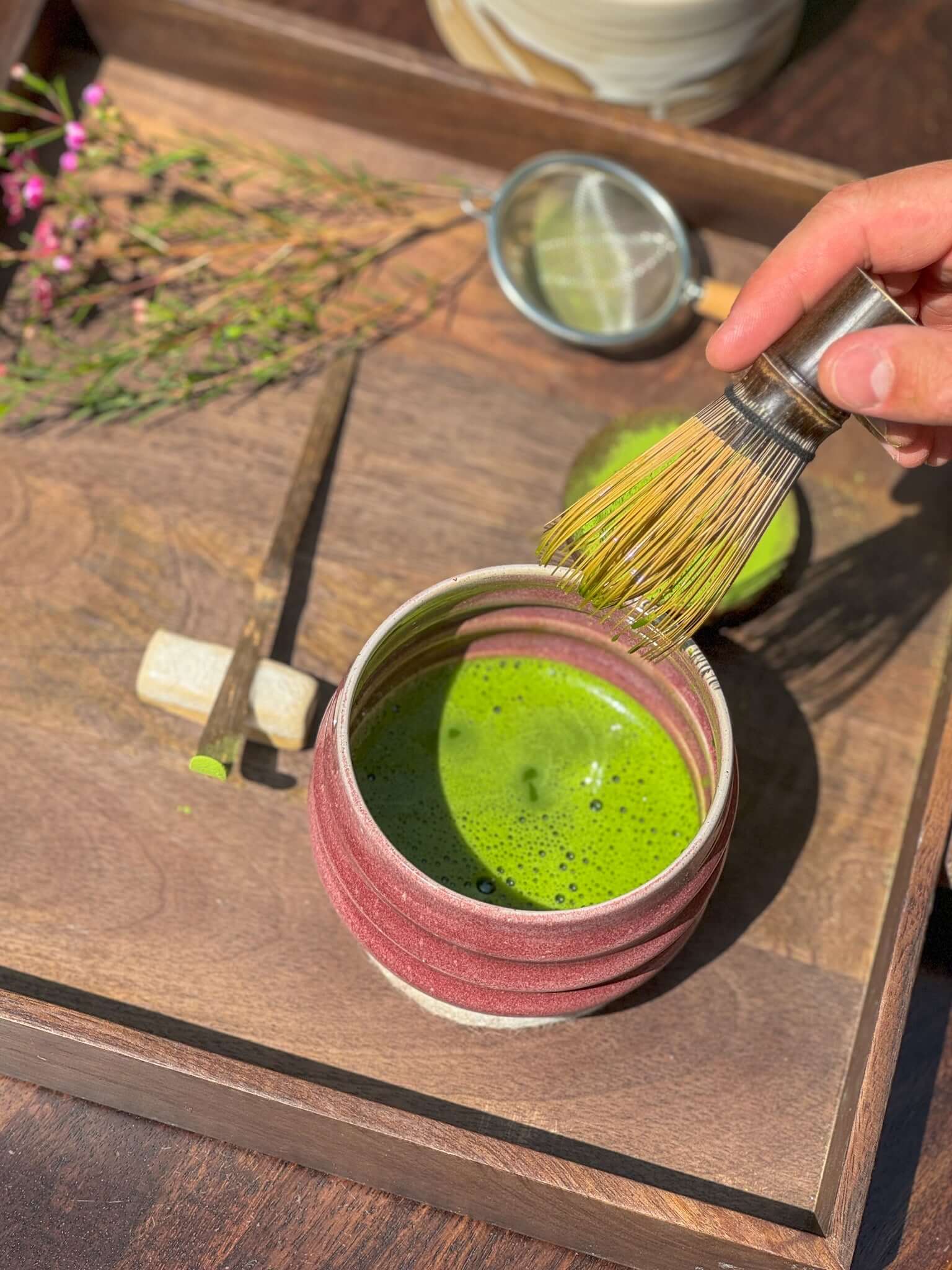 Hand whisking matcha in Ume Series #02 bowl with Japanese aesthetics on wooden tray, symbolizing resilience and renewal.