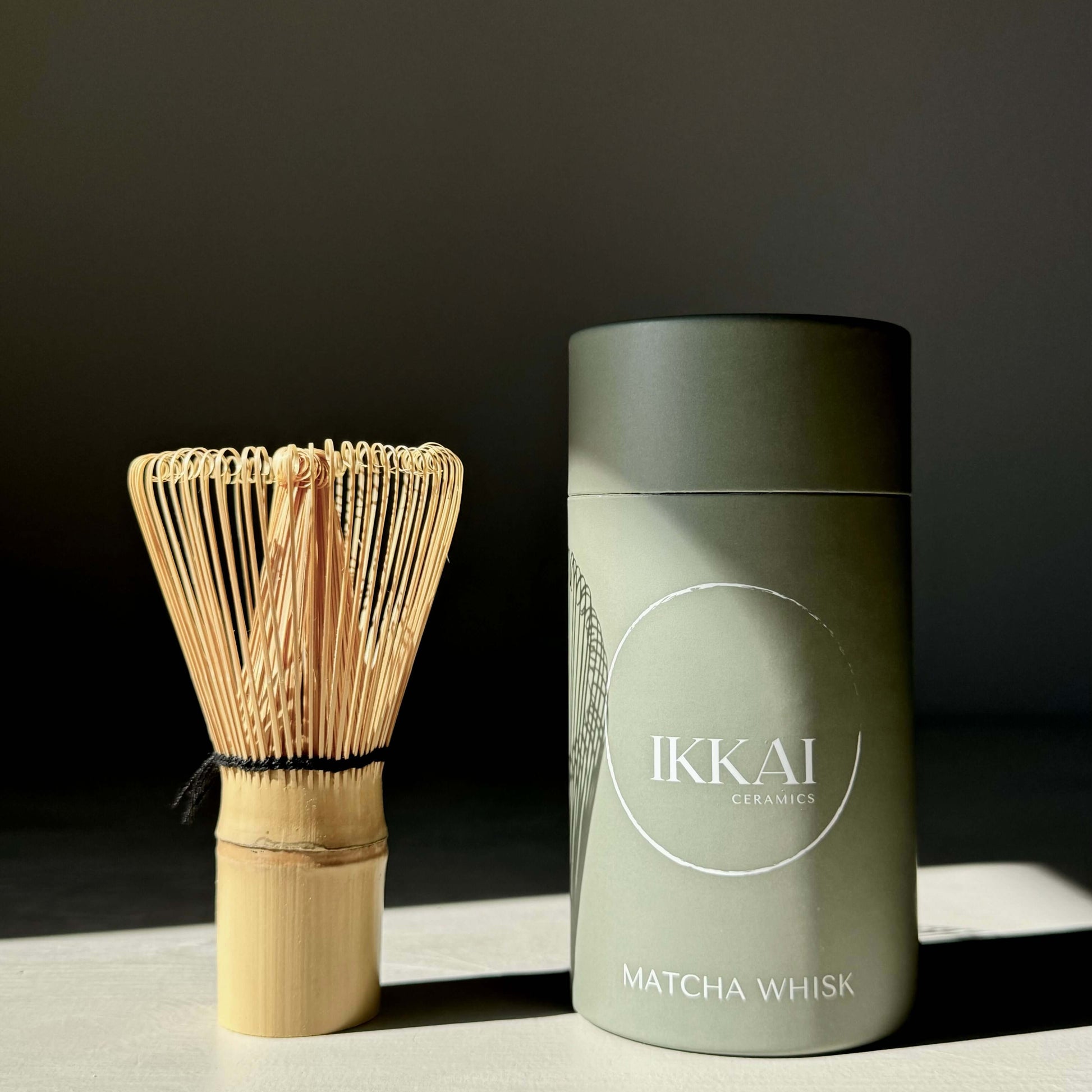 Bamboo matcha whisk (chasen) beside Ikkai ceramics packaging, essential for preparing frothy, creamy matcha tea.