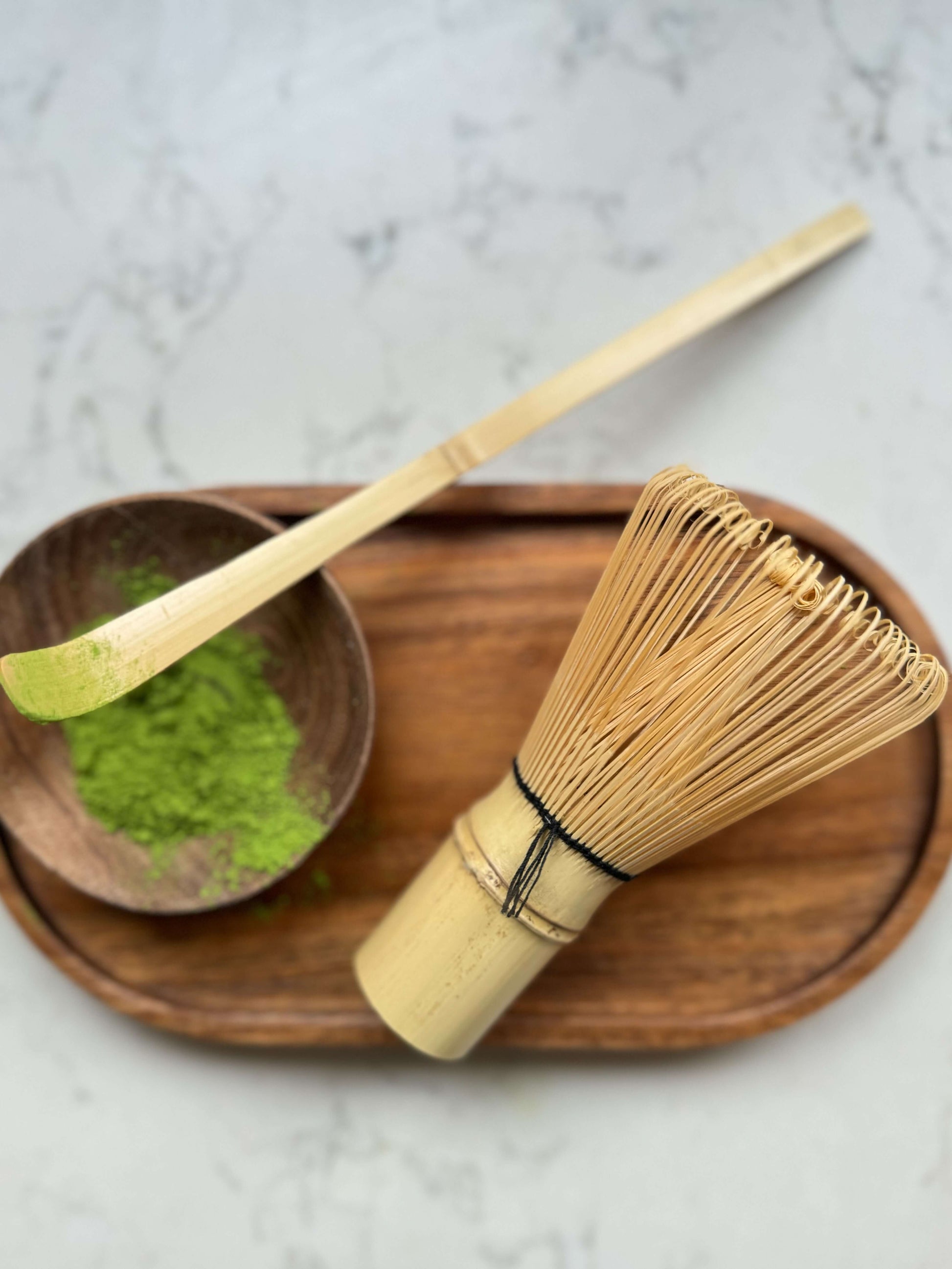 Bamboo matcha whisk (chasen) and matcha powder on a wooden tray for making smooth, frothy green tea.