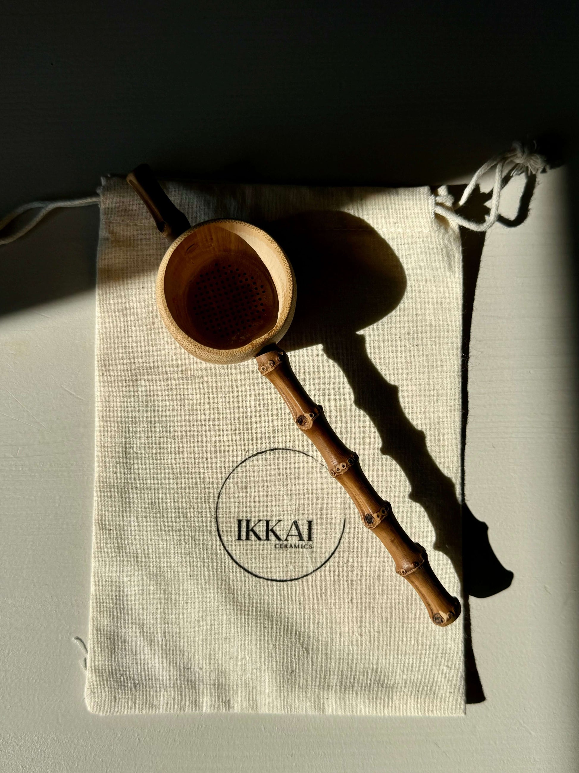 Handcrafted Bamboo Tea Strainer on fabric pouch, perfect for straining tea with rustic charm, adds elegance near handmade ceramic mugs