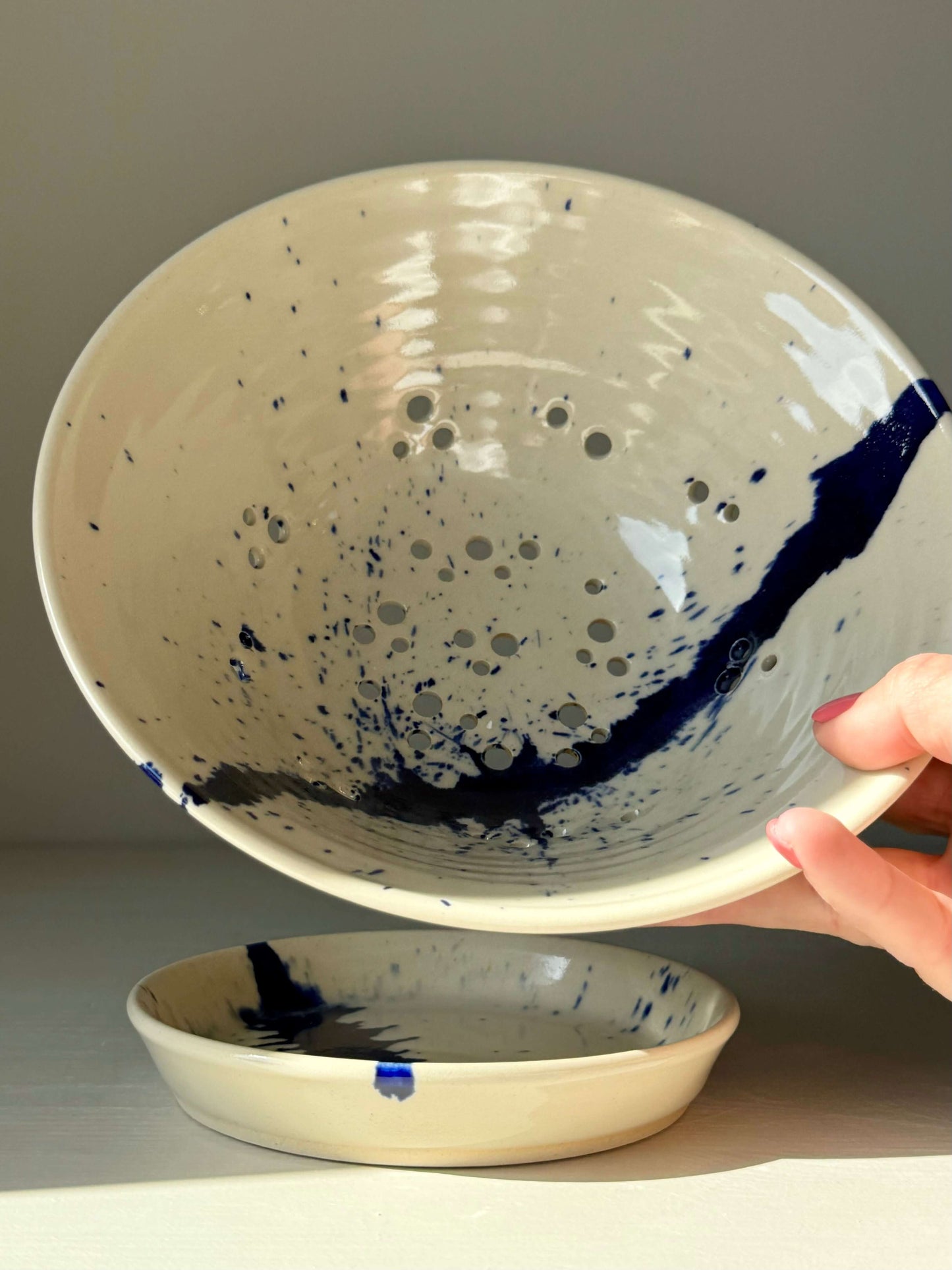 Hand holding sculptural Berry Bowl from the Gosu Series with cobalt blue splashes, designed for rinsing and serving fresh fruit.