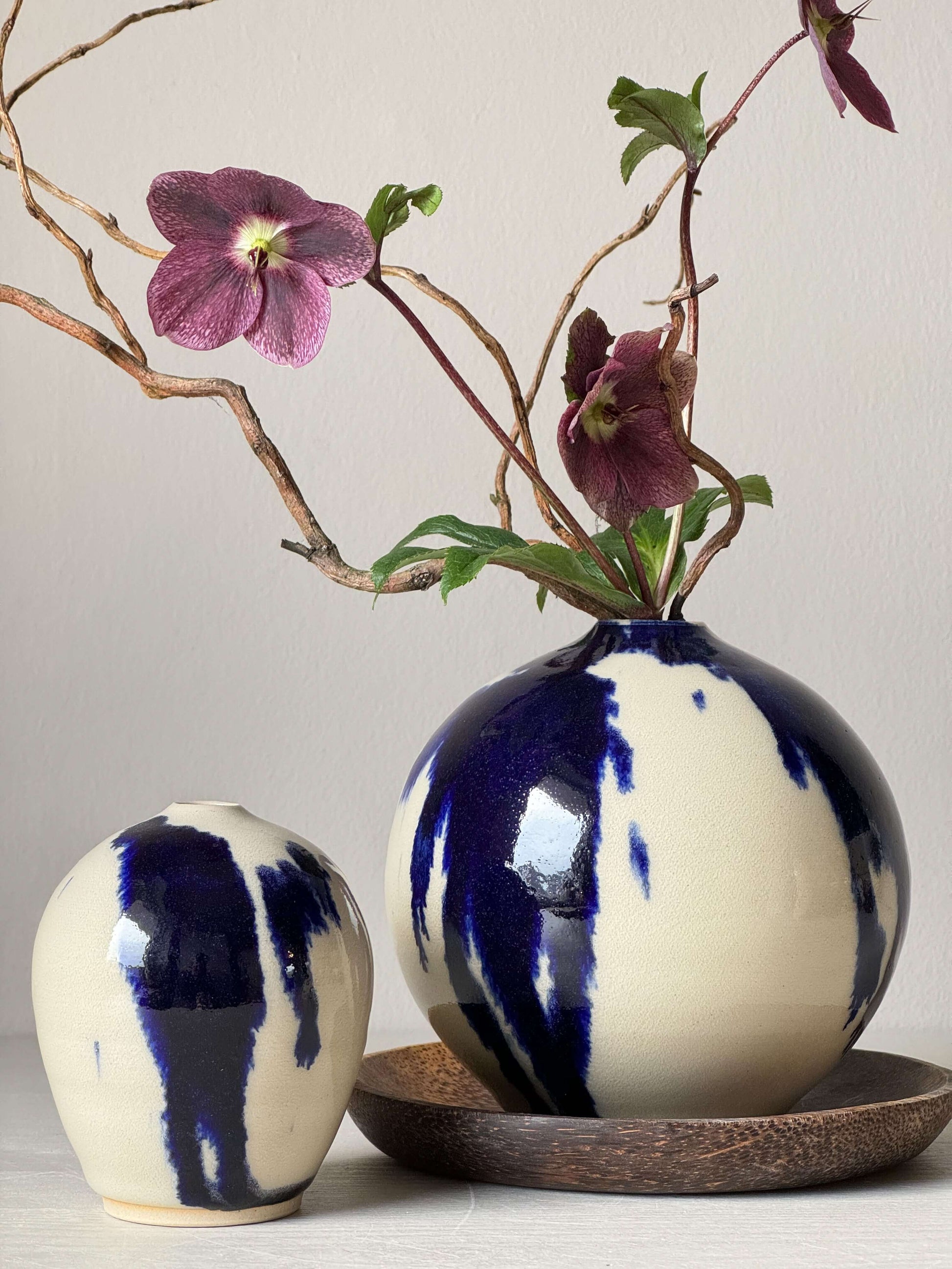 Elegant blue and white ceramic vases with purple flowers, displayed on a natural coconut wood side plate, showcasing organic design.