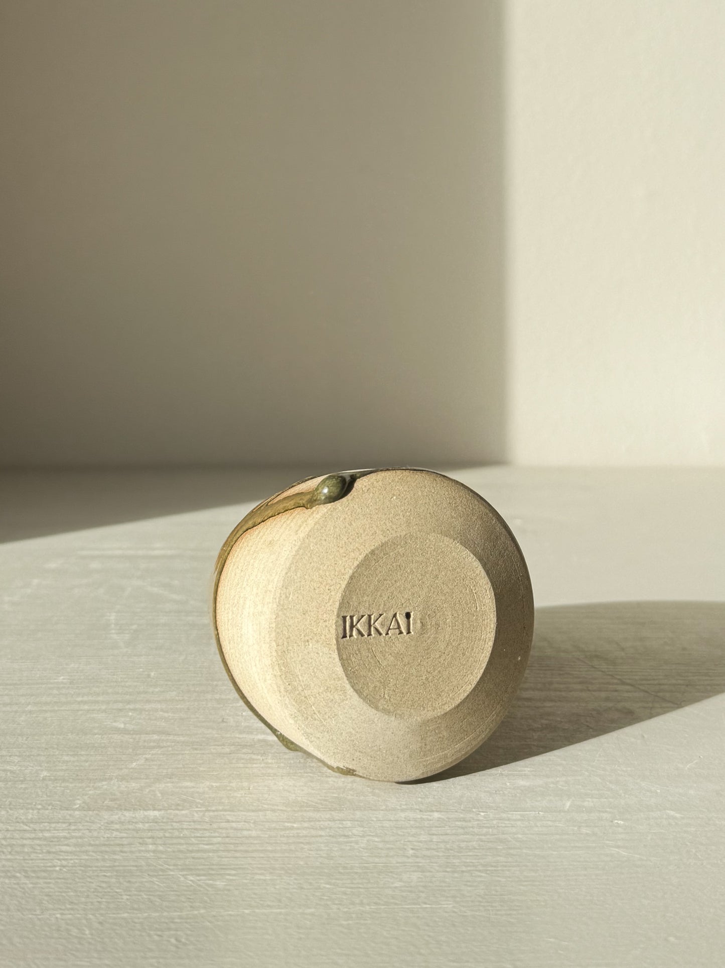 Simple ceramic object with 'IKKAI' engraved, showcasing minimalist design on a light surface.