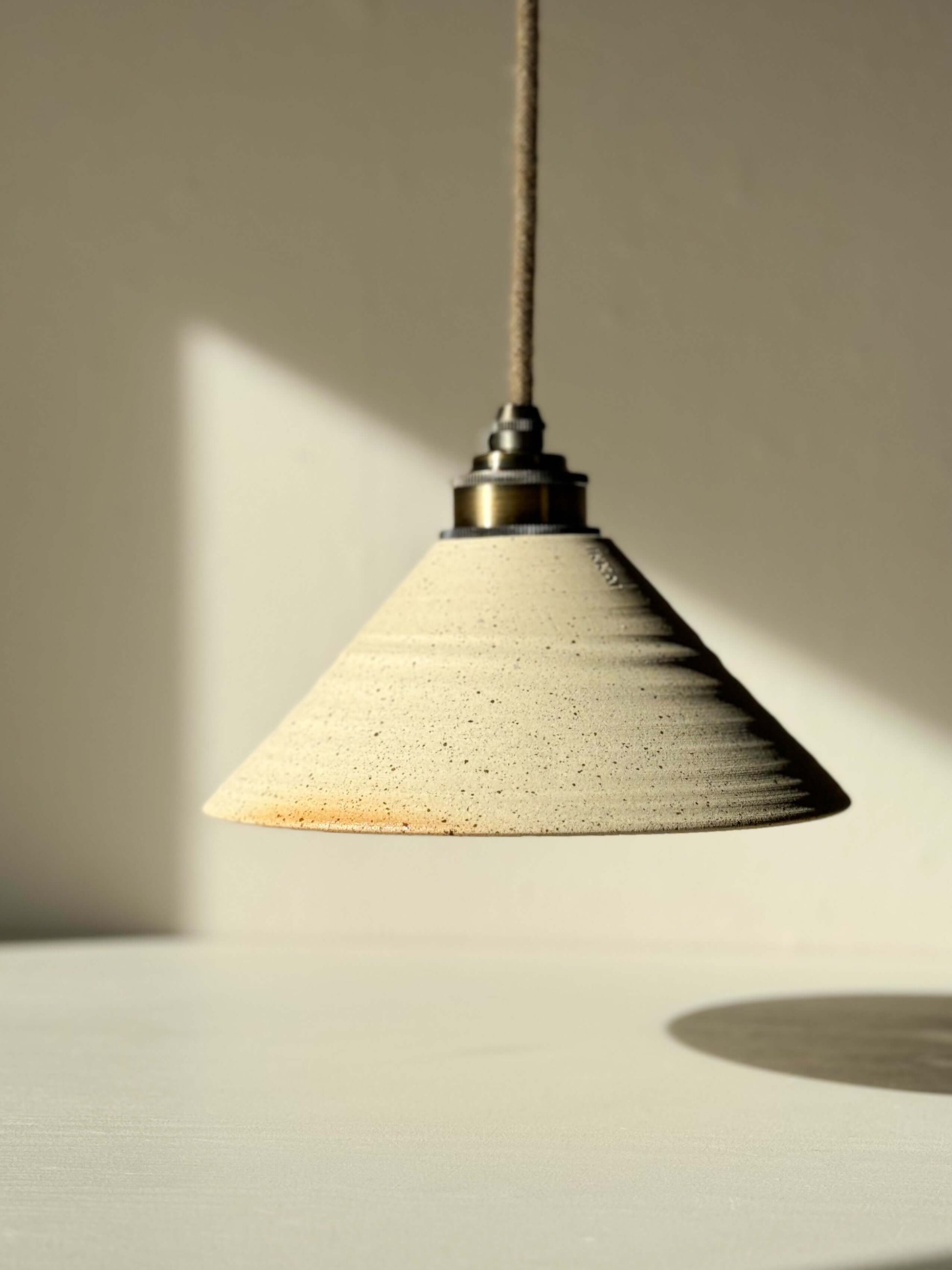 Ceramic lamp shade with half clear glaze, showcasing raw clay texture and sleek interior reflection, hanging in natural light.