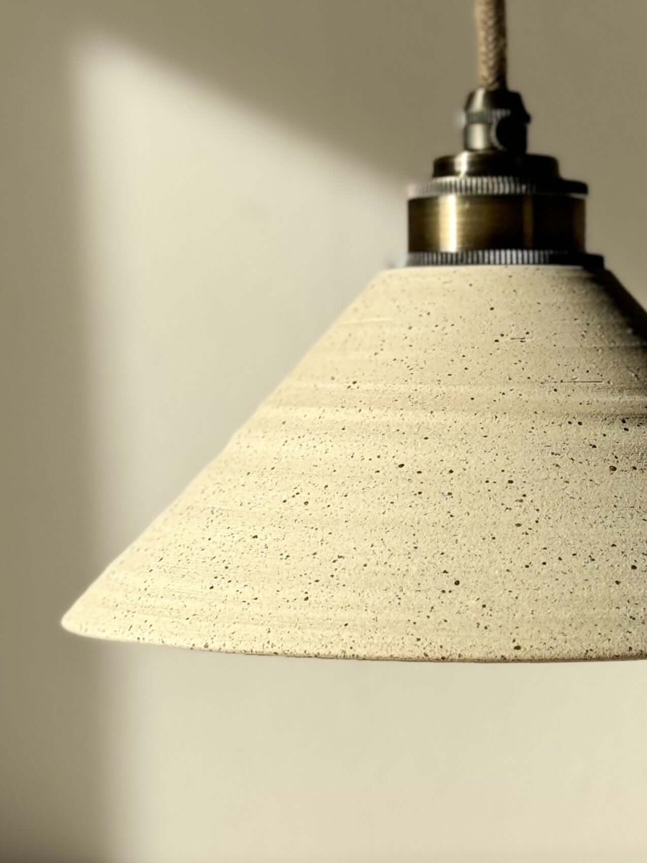 Ceramic lamp shade with half clear glaze, featuring unglazed matte exterior and smooth interior, hanging in warm light.
