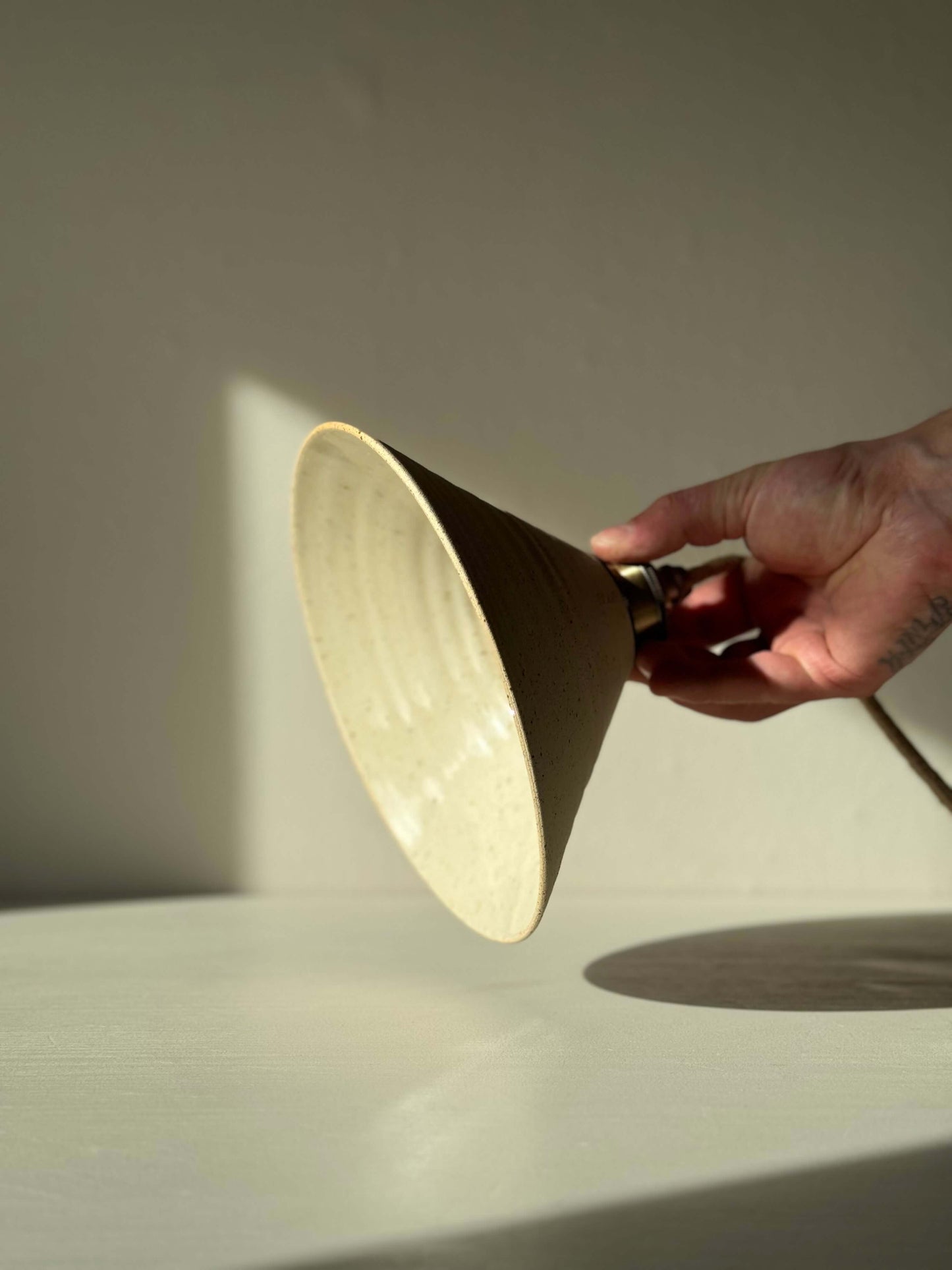 Hand holding Ceramic Lamp Shade with half clear glaze, showcasing the raw matte clay exterior and reflective glazed interior.