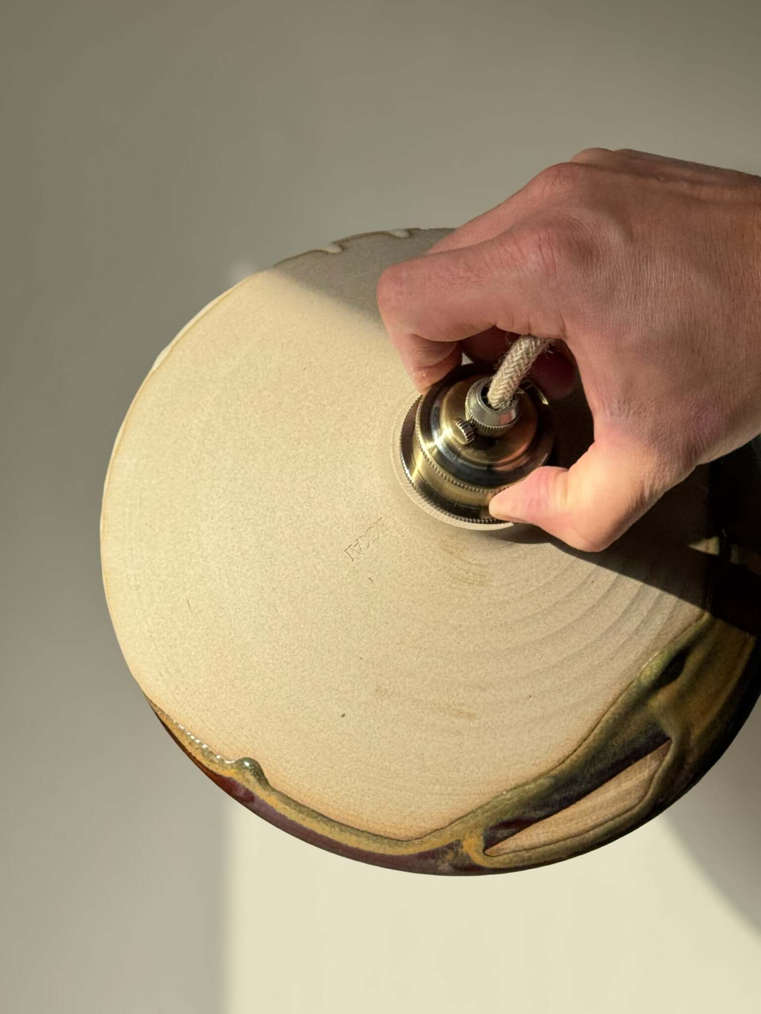 Hand adjusting a handmade Ceramic Lamp Shade – Inyo #02, highlighting the raw clay texture and natural glaze drips.
