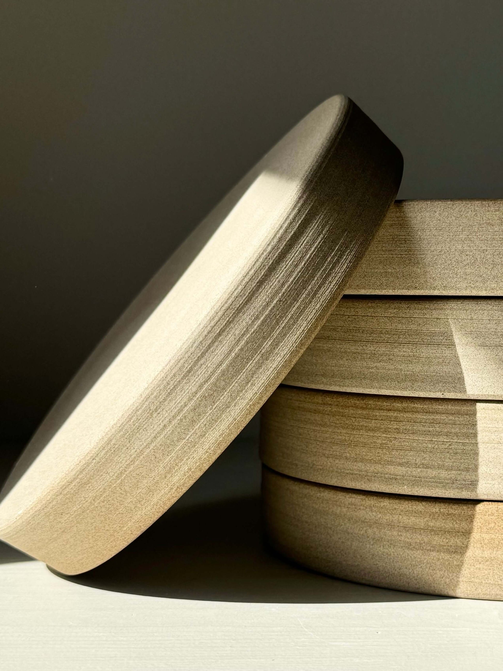 Wheel-thrown ceramic plates from the Yuki Series with toffee-colored clay and glossy white glaze, stacked in soft light.