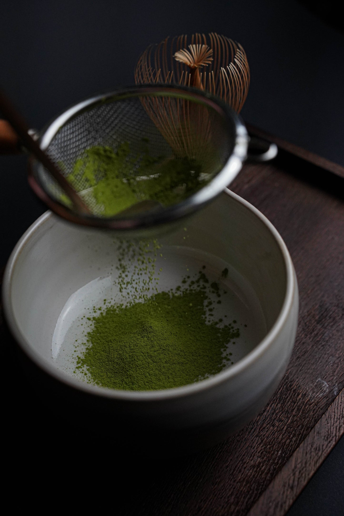 Sifting Fuji Matcha – Japan (Ceremonial Grade) into a bowl with chasen whisk on a wooden tray.