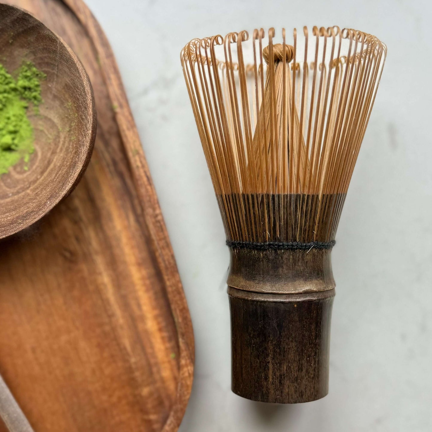 Dark brown bamboo matcha whisk (Chasen) on a wooden tray, used for traditional tea ceremonies.