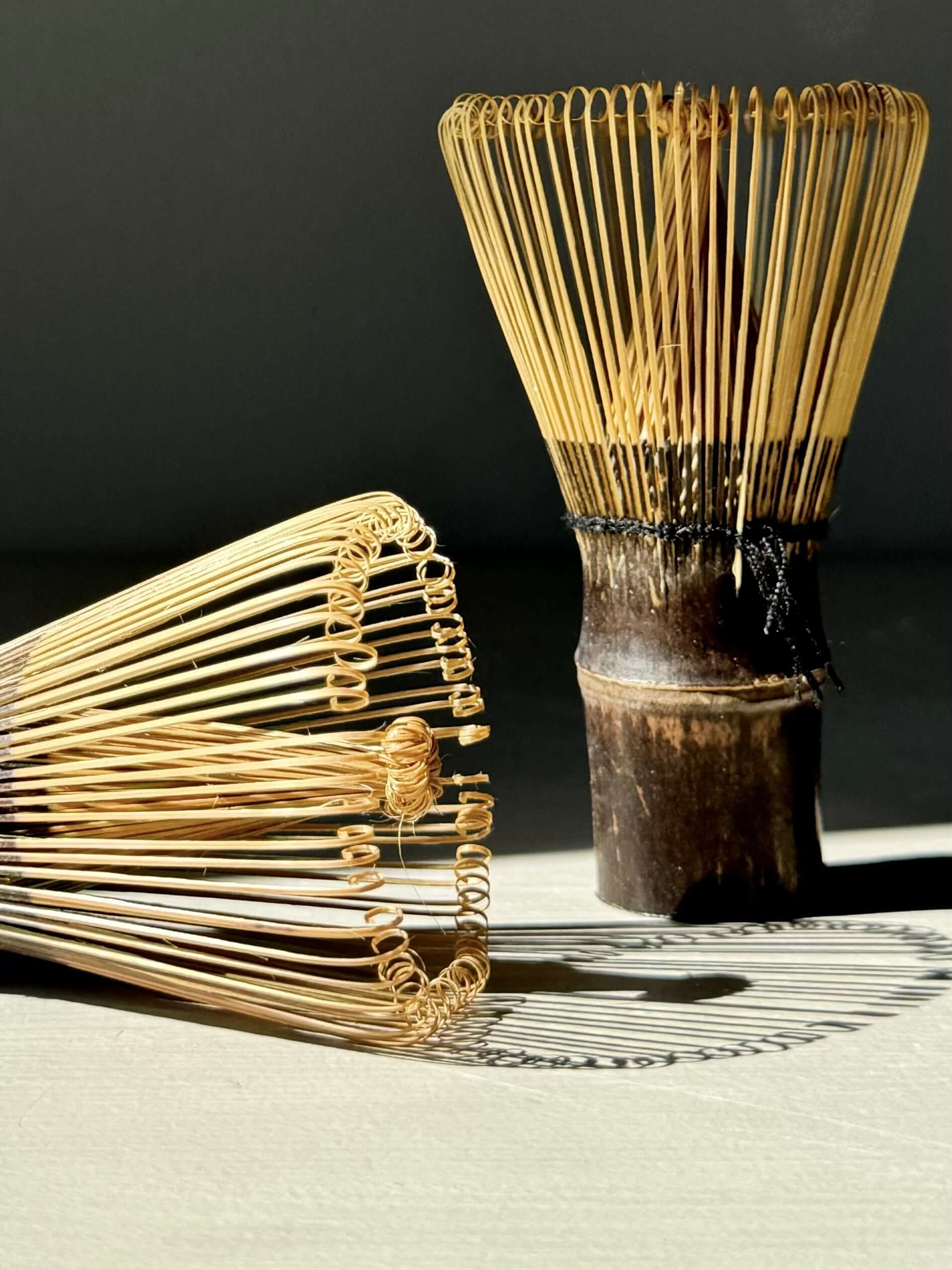 Dark brown bamboo matcha whisks (Chasen) on a light background, showcasing elegant carved tines for tea rituals.