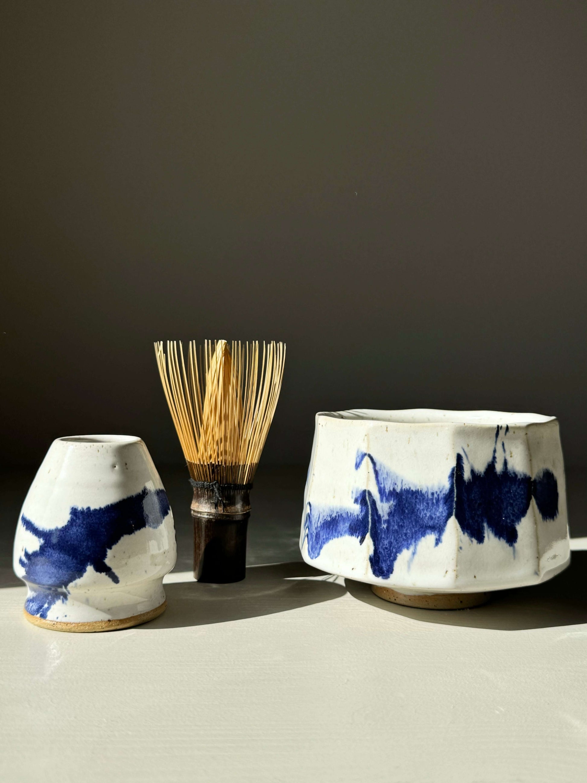 Faceted Matcha Bowl in glossy white glaze with cobalt blue accents, accompanied by a bamboo whisk.