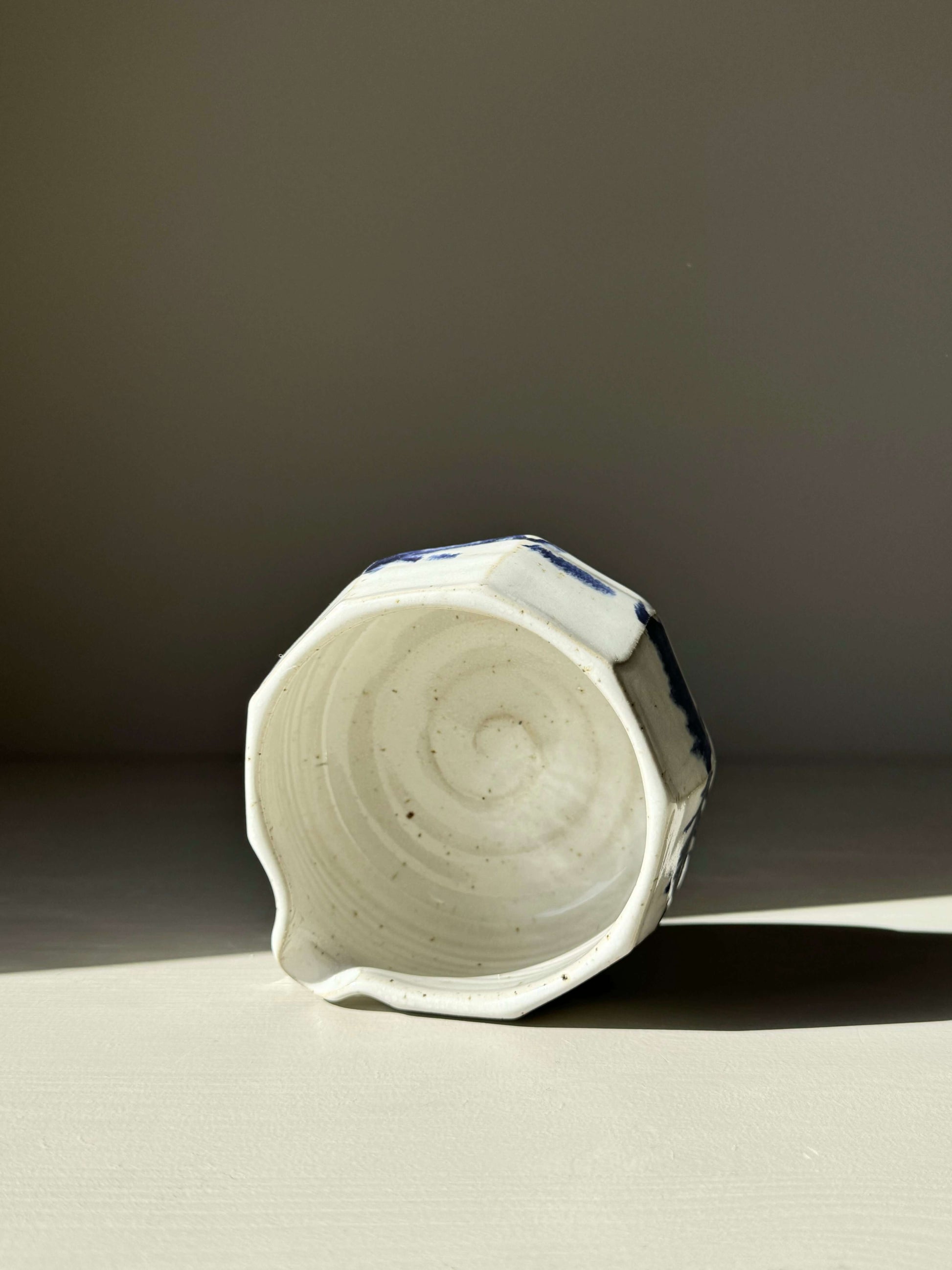 Faceted matcha bowl with a cobalt blue spout and glossy white glaze, showcasing its textured interior and unique design.