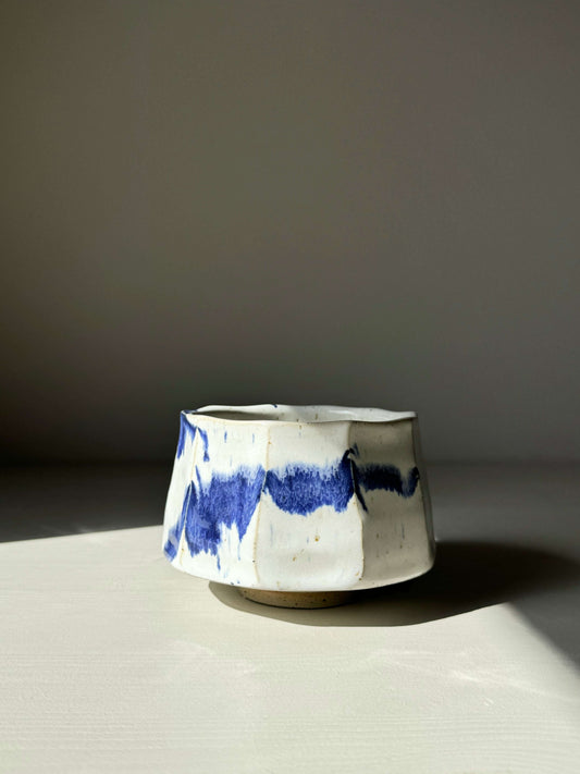 Faceted matcha bowl with cobalt blue splashes and glossy white glaze, showcasing a modern design and textured surface.