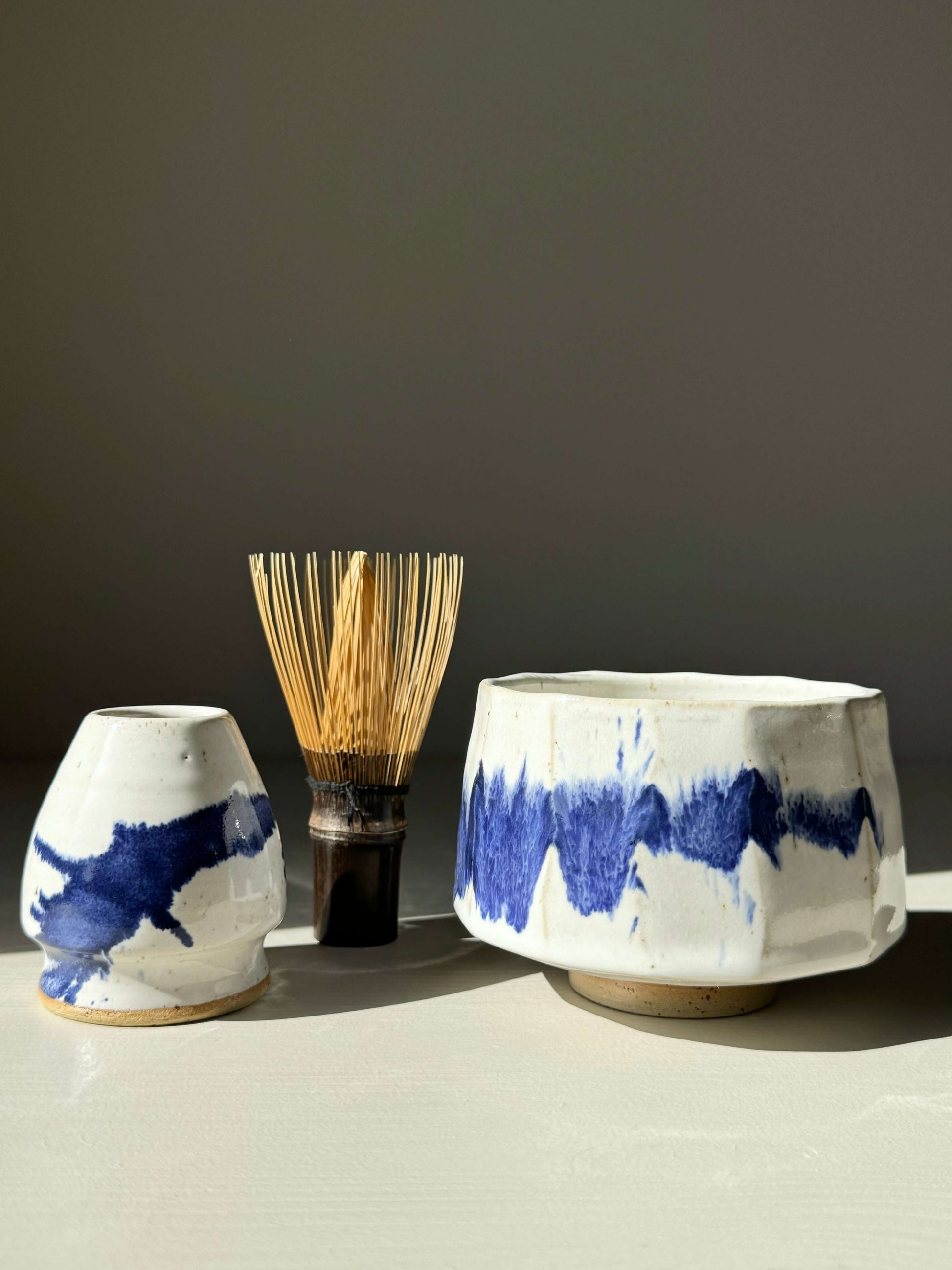 Faceted matcha bowl with cobalt blue accents and bamboo whisk on a light surface.