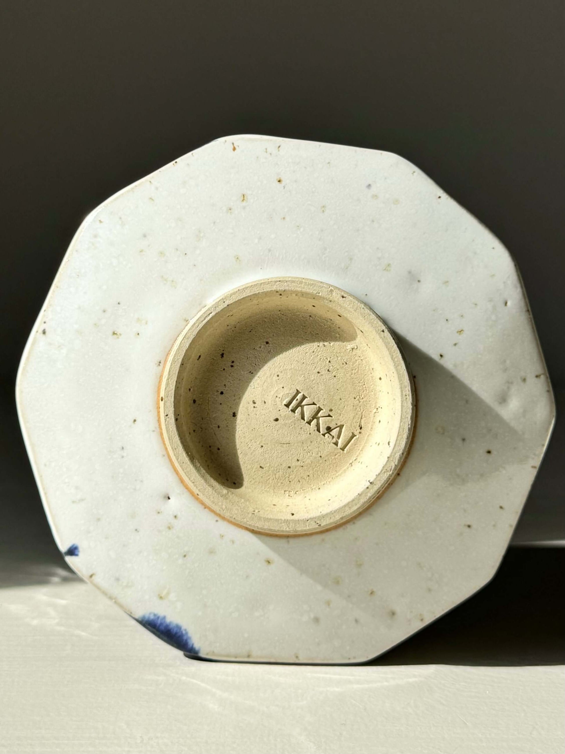 Base of faceted matcha bowl with glossy white glaze and cobalt blue accents, stamped with "IKKA", showcasing textured modern design.