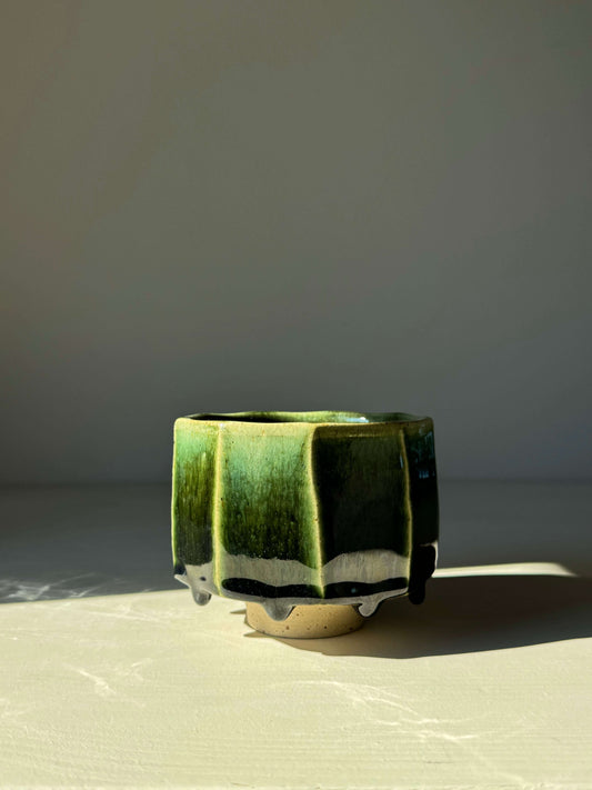 Faceted Matcha Bowl from Hinoki Series with deep green glaze and hand-carved facets, highlighted by sunlight, on display.