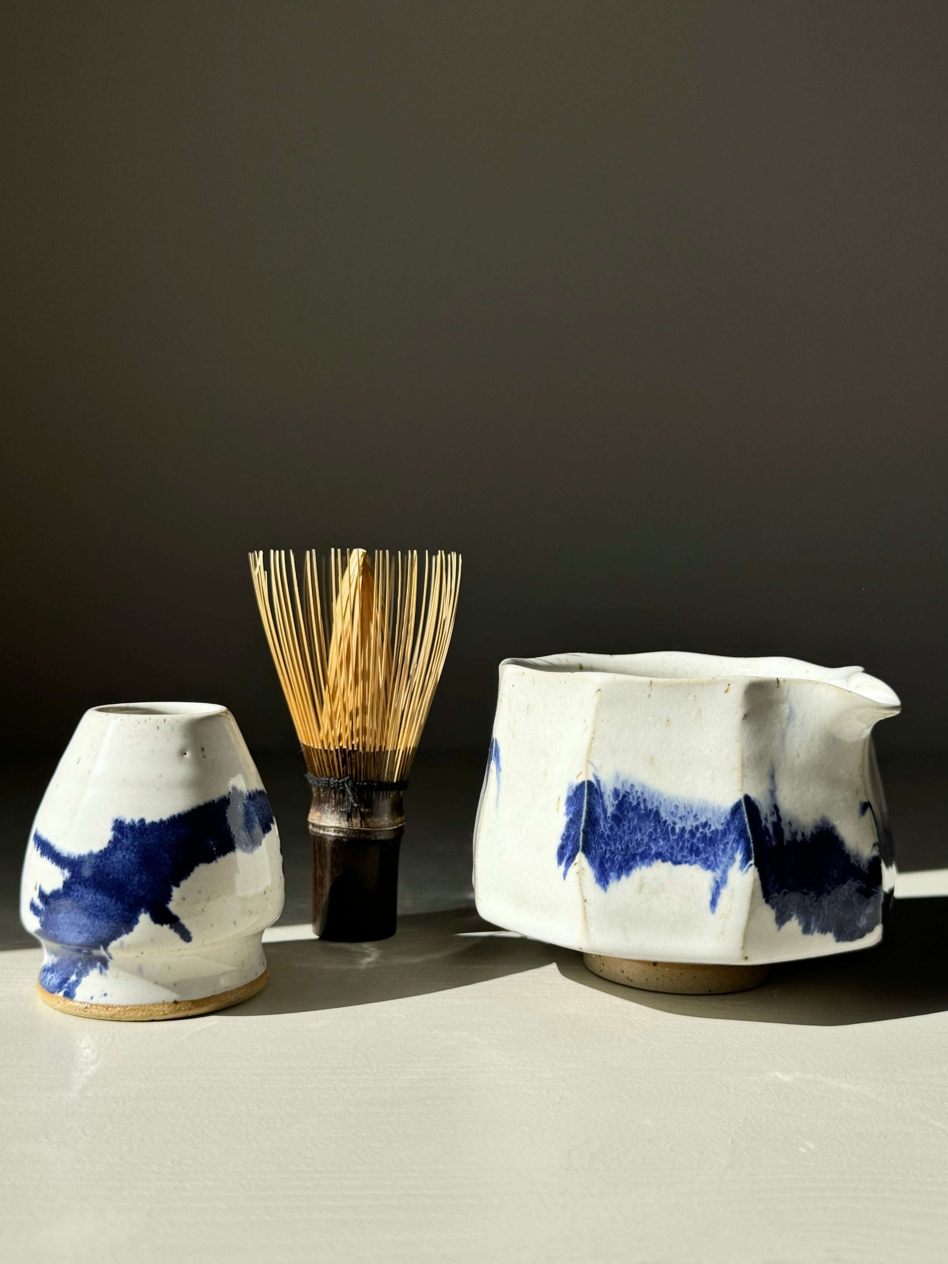 Cobalt Blue & White Faceted Matcha Bowl with Spout, featuring hand-splashed glaze, alongside a bamboo whisk on a gray surface.