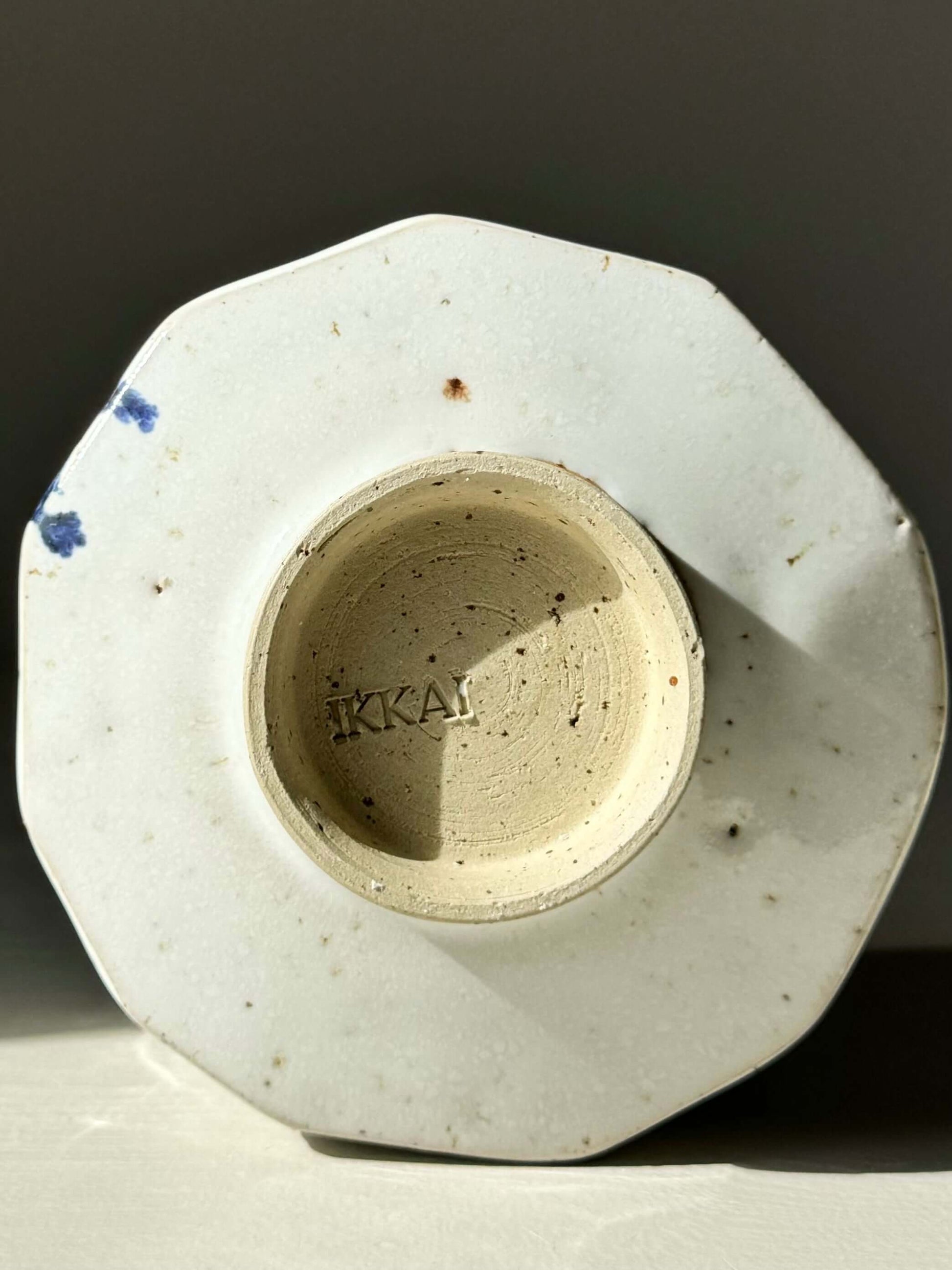Bottom view of a faceted matcha bowl with cobalt blue splashes and glossy white glaze base, showing texture and maker's mark.