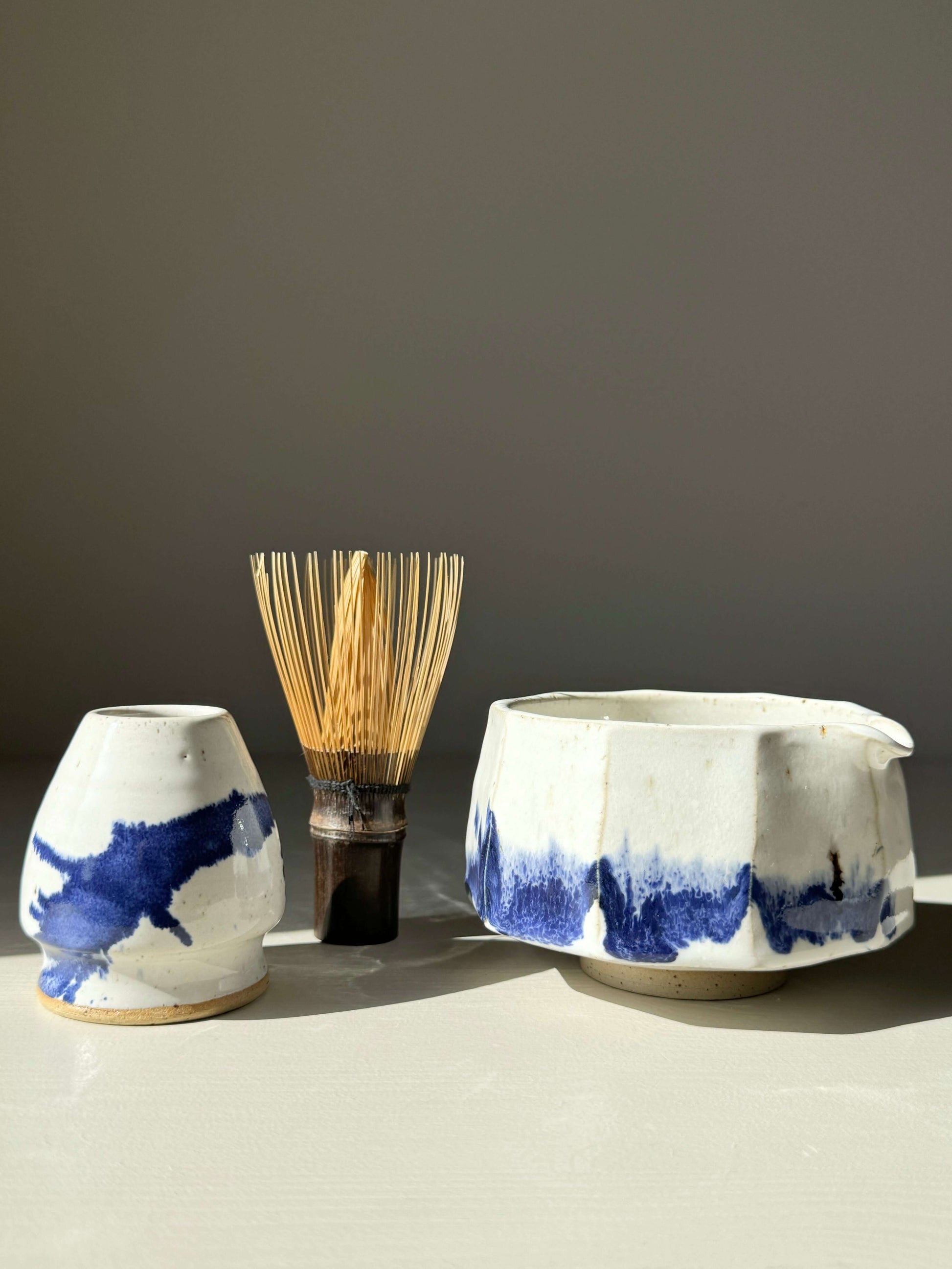 Faceted Matcha Bowl with Spout in cobalt blue, glossy white glaze, paired with a bamboo whisk, showcasing modern design and texture.