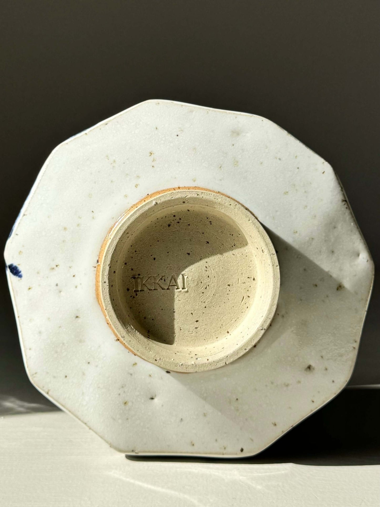 Bottom view of faceted matcha bowl with glossy white glaze, showing texture and design detail, marked 'KKA1'.