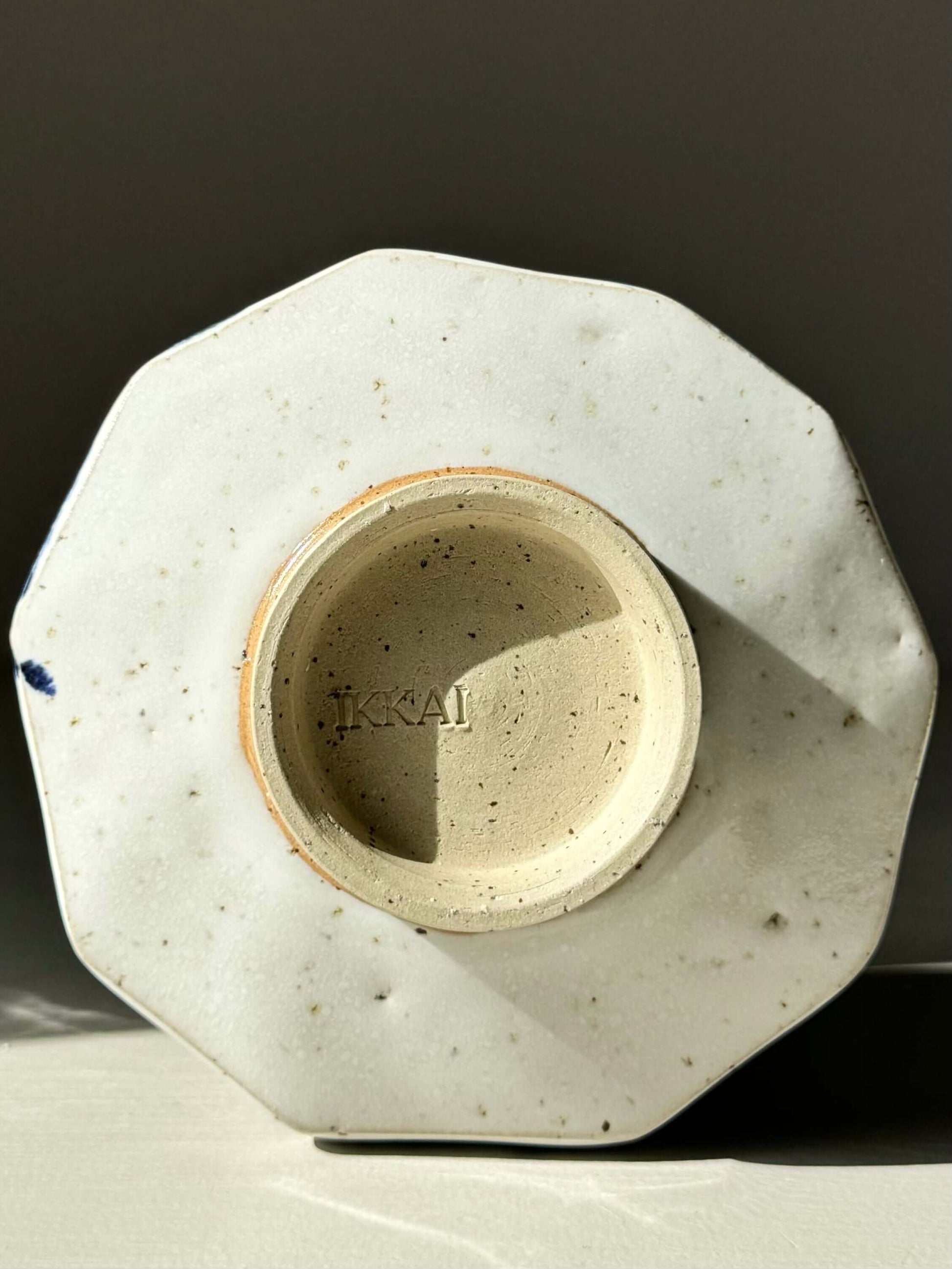 Bottom view of faceted matcha bowl with glossy white glaze, showing texture and design detail, marked 'KKA1'.