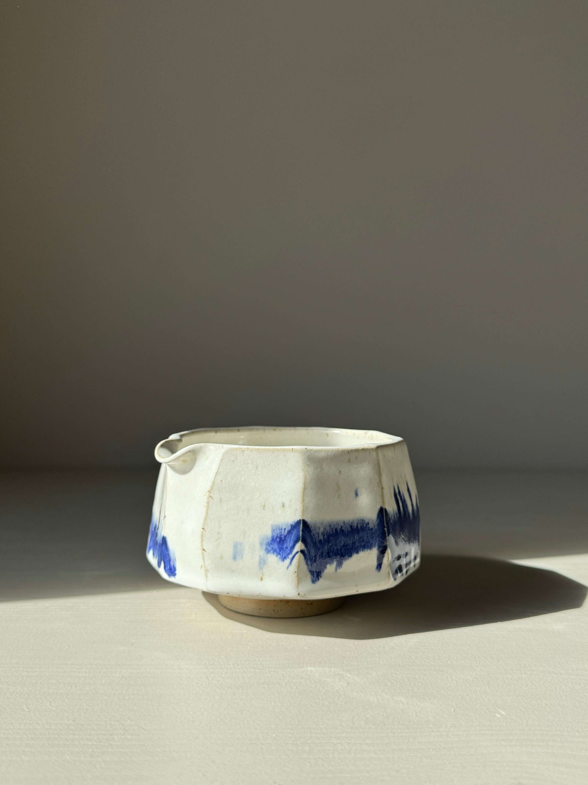 Faceted matcha bowl with spout, featuring glossy white glaze and cobalt blue accents, modern design.
