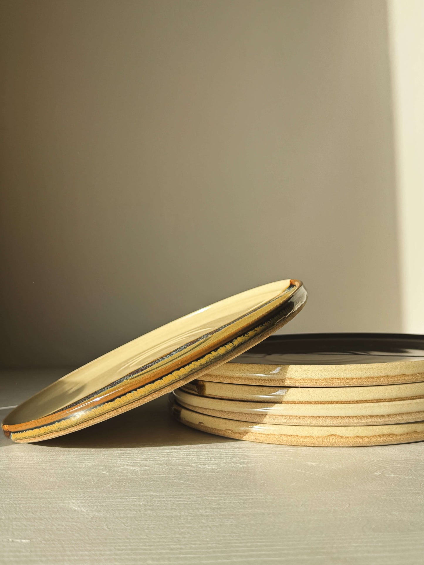 Stack of Flat Round Breakfast Plate – Inyo with tenmoku and clear glaze, set on a light surface.