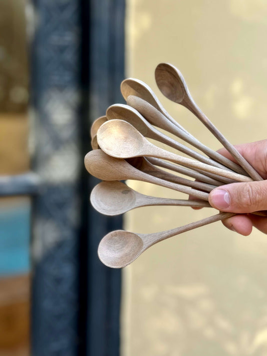 Bundle of hand-carved walnut tea spoons held in a hand, showcasing natural wood craftsmanship from Marrakech.