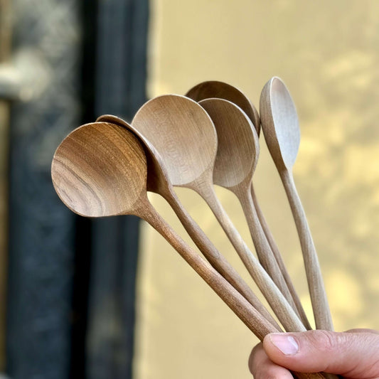 Hand holding a set of hand-carved walnut wood serving spoons, showcasing unique grain patterns, crafted by artisans in Marrakech.