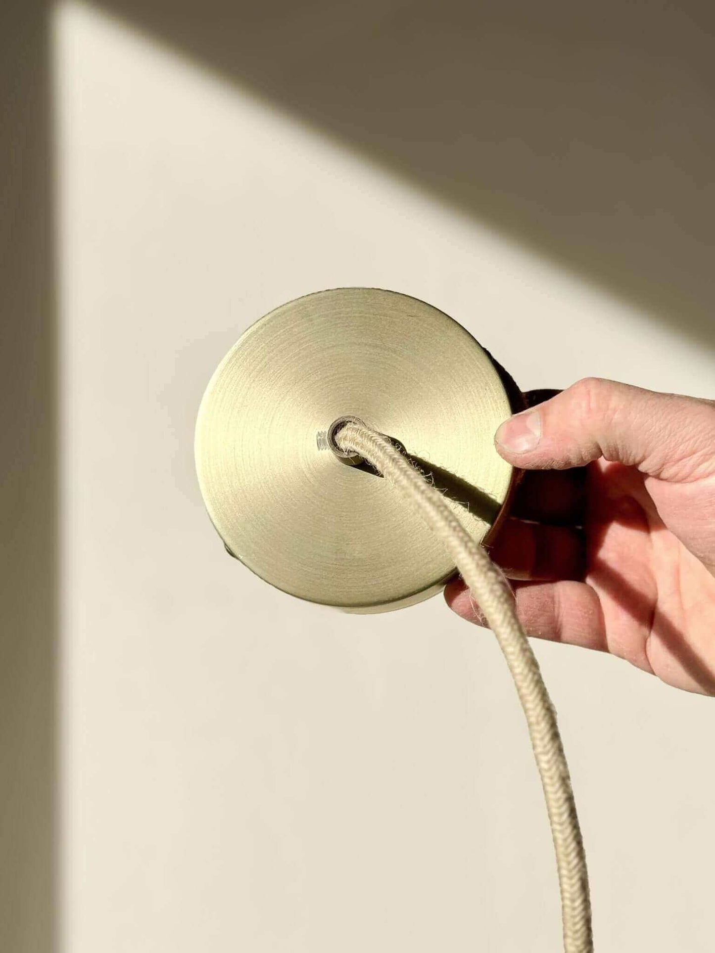 Hand holding round brass light fixture part with cord in sunlight
