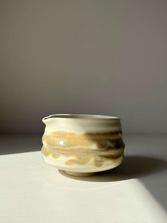 Hand-thrown matcha bowl with spout, clear glaze, and tenmoku splashes, featuring unique grooves and earthy tones.