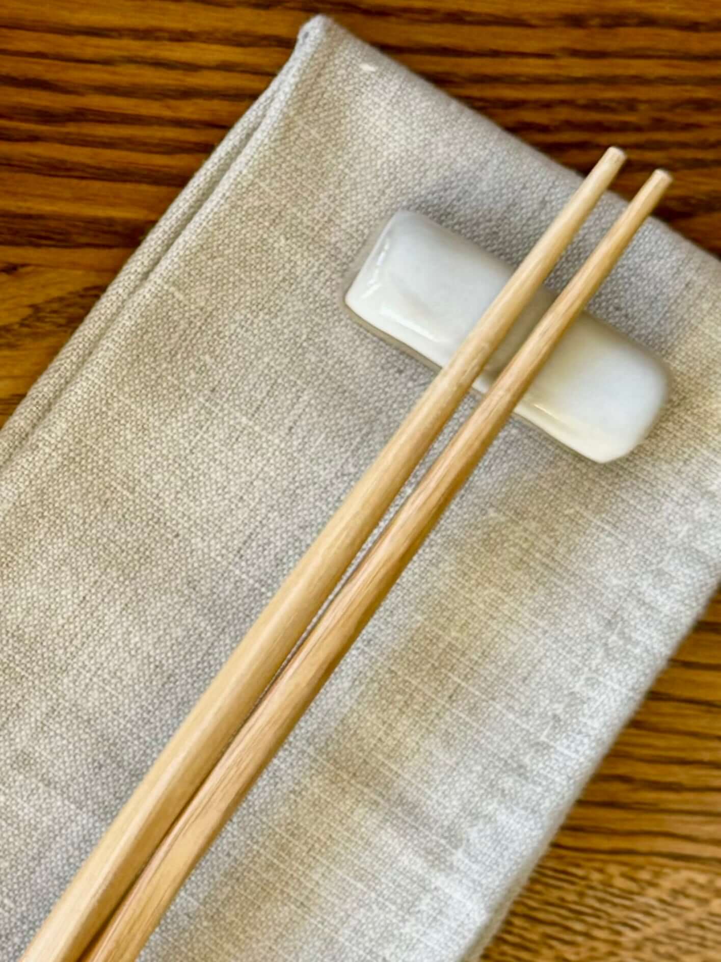 Handmade ceramic Chopstick/Spoon Rest – Yuki on a beige cloth with wooden chopsticks, showcasing unique white glaze design.