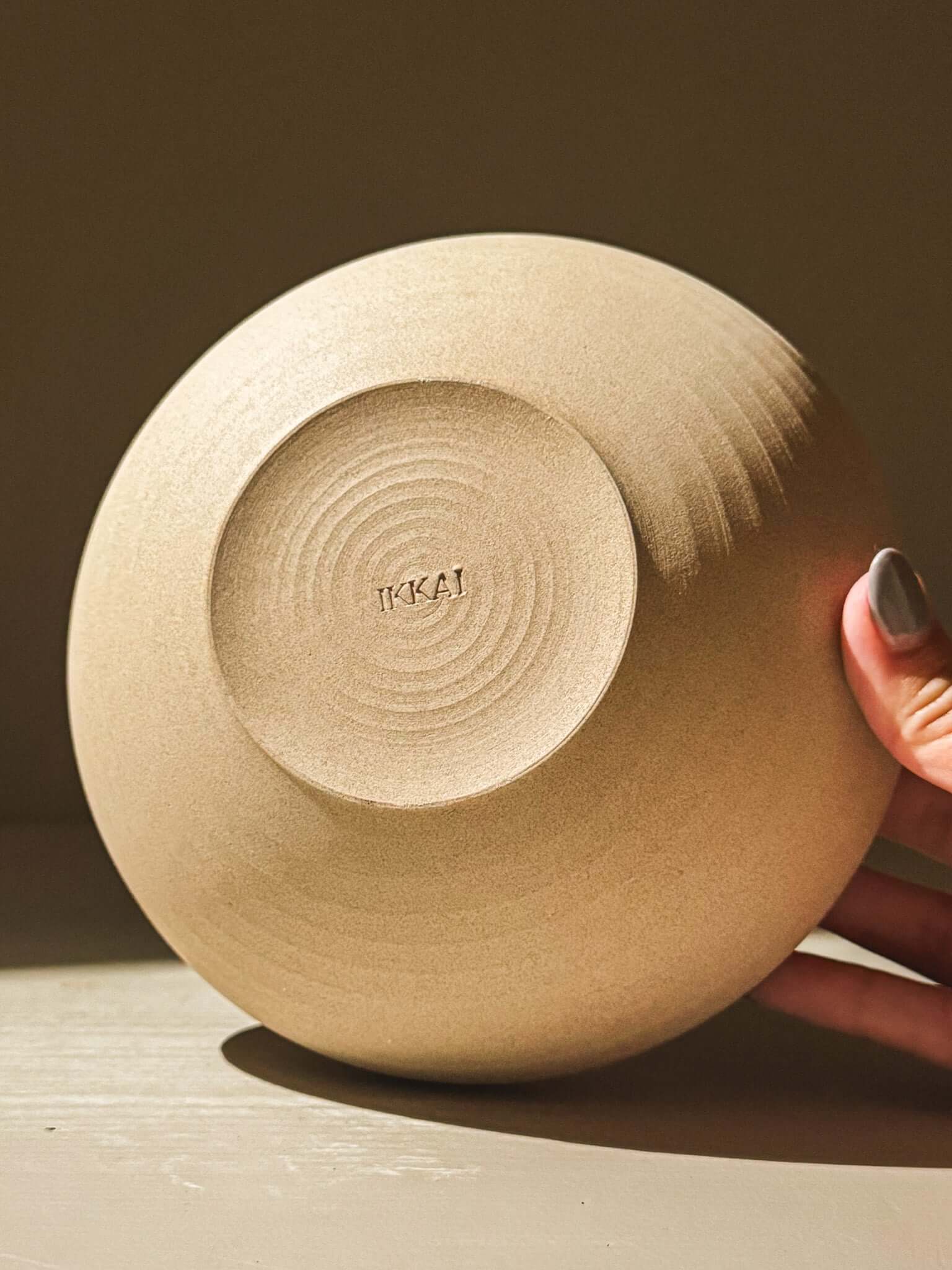 Hand holding handmade stoneware double-walled bowl with toffee-toned clay and gentle throwing lines, part of the Inyo Series.