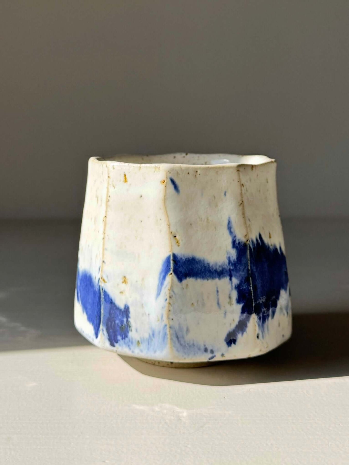 Handmade Faceted Cup – Cobalt Blue & Glossy White #01 ceramic with unique glaze pattern on table.