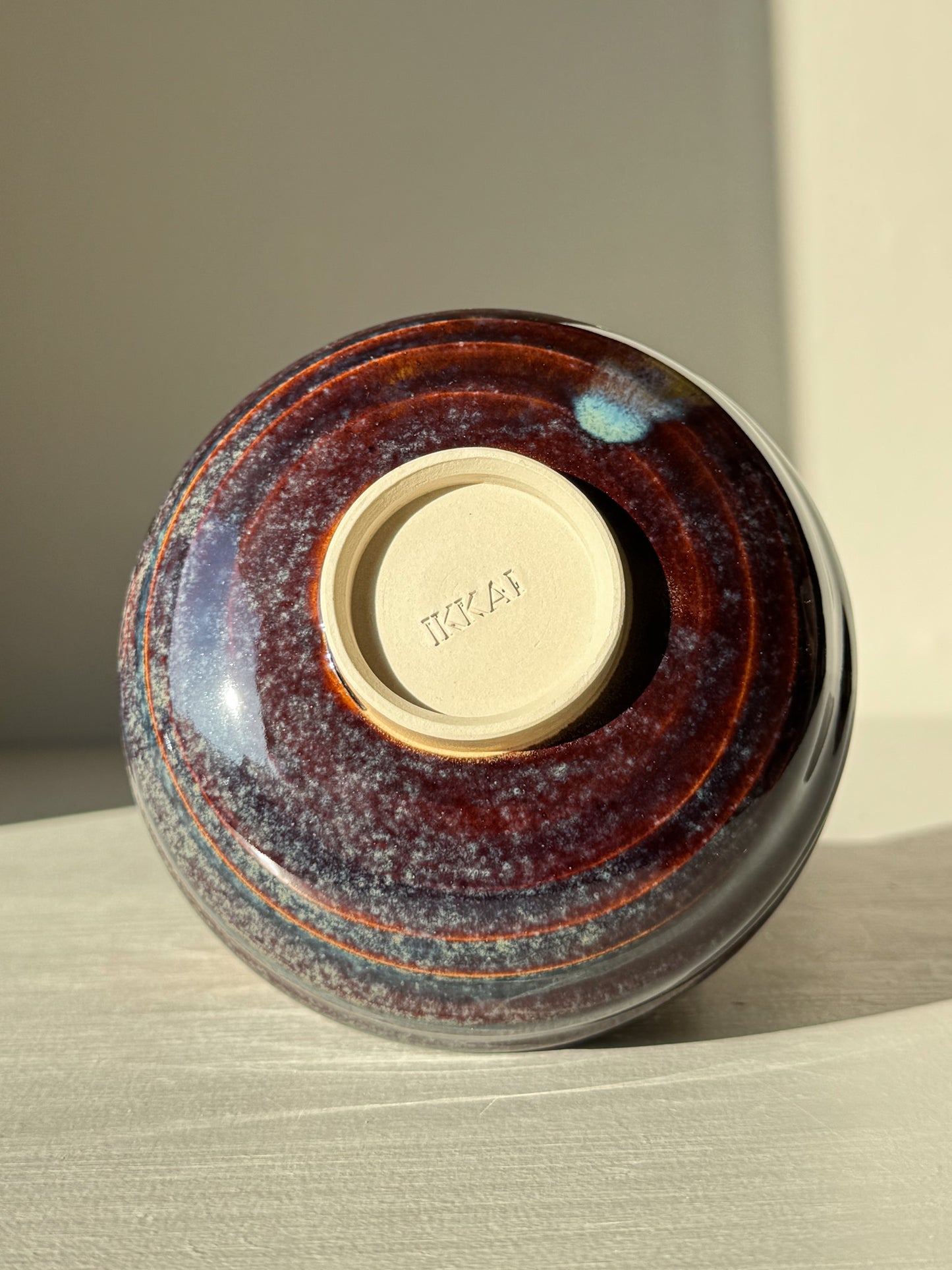 Underside of Matcha Bowl - Glossy Blue #02 showing earthy tones and circular base on a light surface.