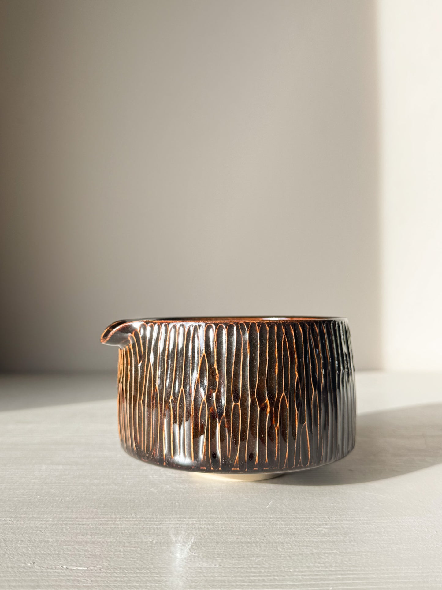 Matcha Bowl Spout – Kinsei #01 with hand-carved vertical lines and glossy glaze, deep brown and golden highlights, on display.