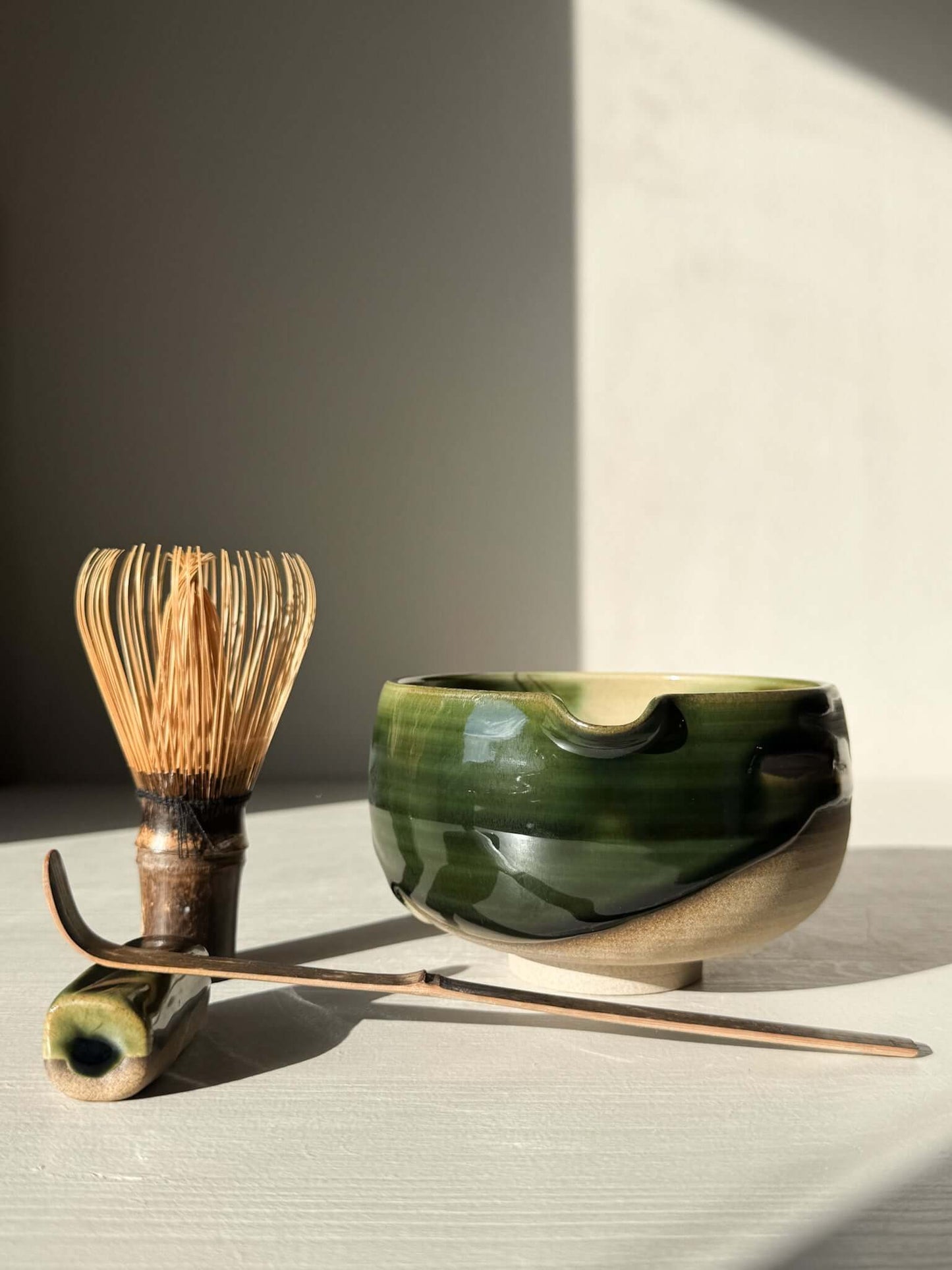 Matcha Bowl with Spout – Mori #05, handmade ceramic with green and brown glaze, displayed with whisk and scoop on a light surface.