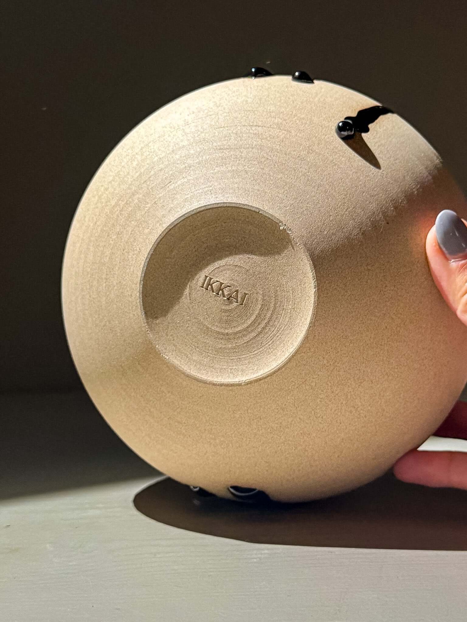 Hand holding the base of an Orb Vase – Kuro #01, showcasing its unique clay texture and round shape.