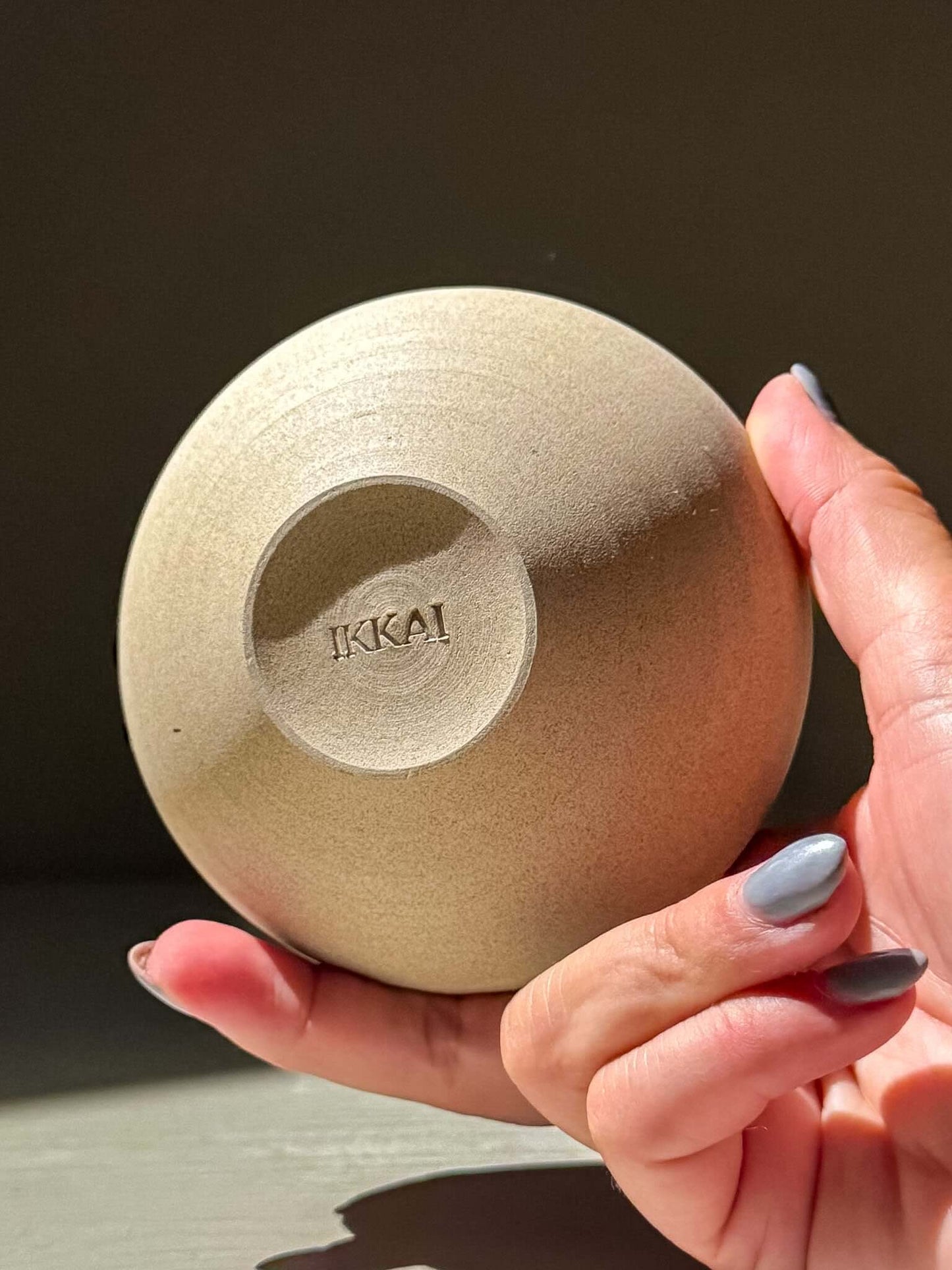 Hand holding a Japanese handmade ceramic orb vase, Orb Vase – Kuro #04, showcasing its smooth surface and unique texture.