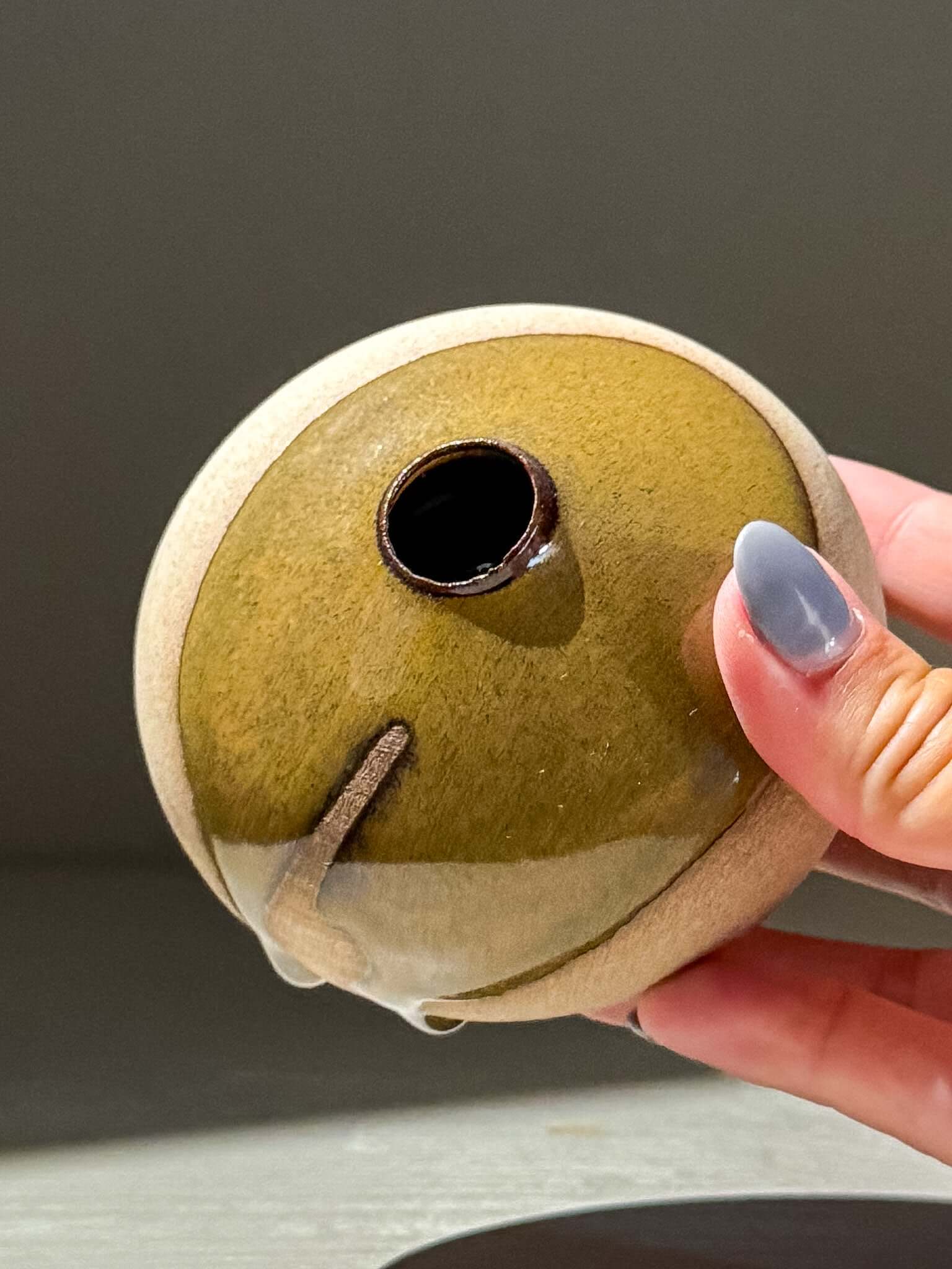 Hand holding an Orb Vase – Tenmoku #15 showcasing its unique glaze and handmade ceramics design.