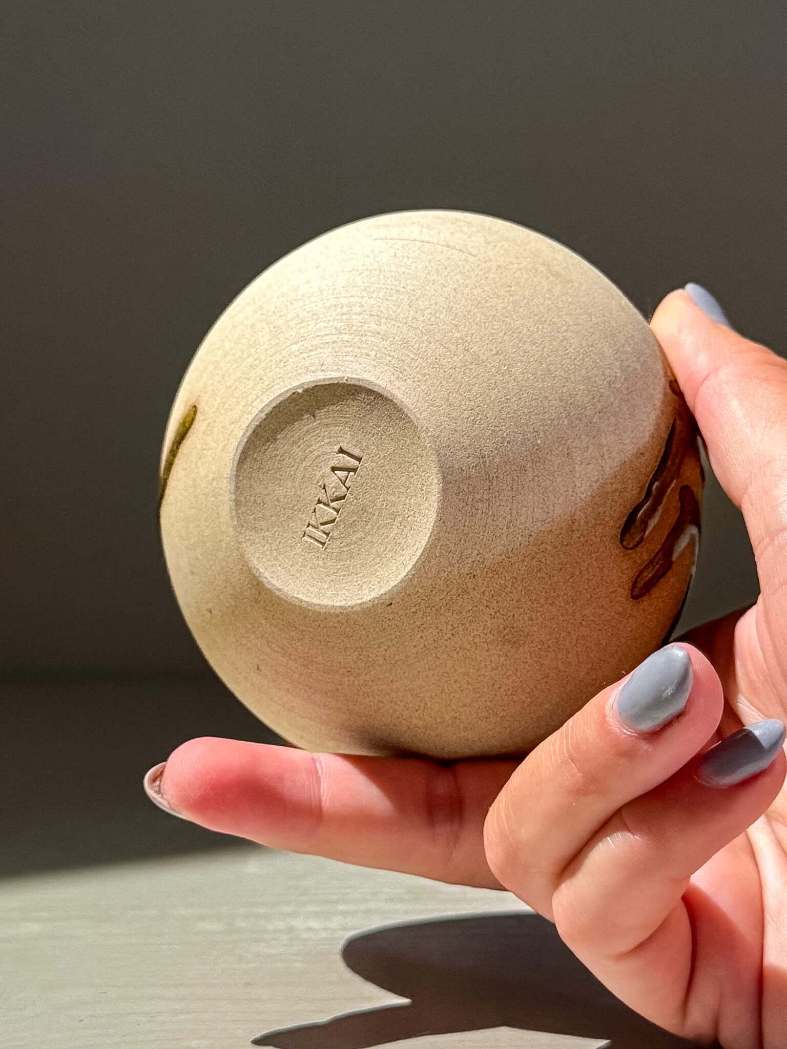 Handmade Orb Vase – Tenmoku #13 in a hand, showcasing unique glaze and round shape.