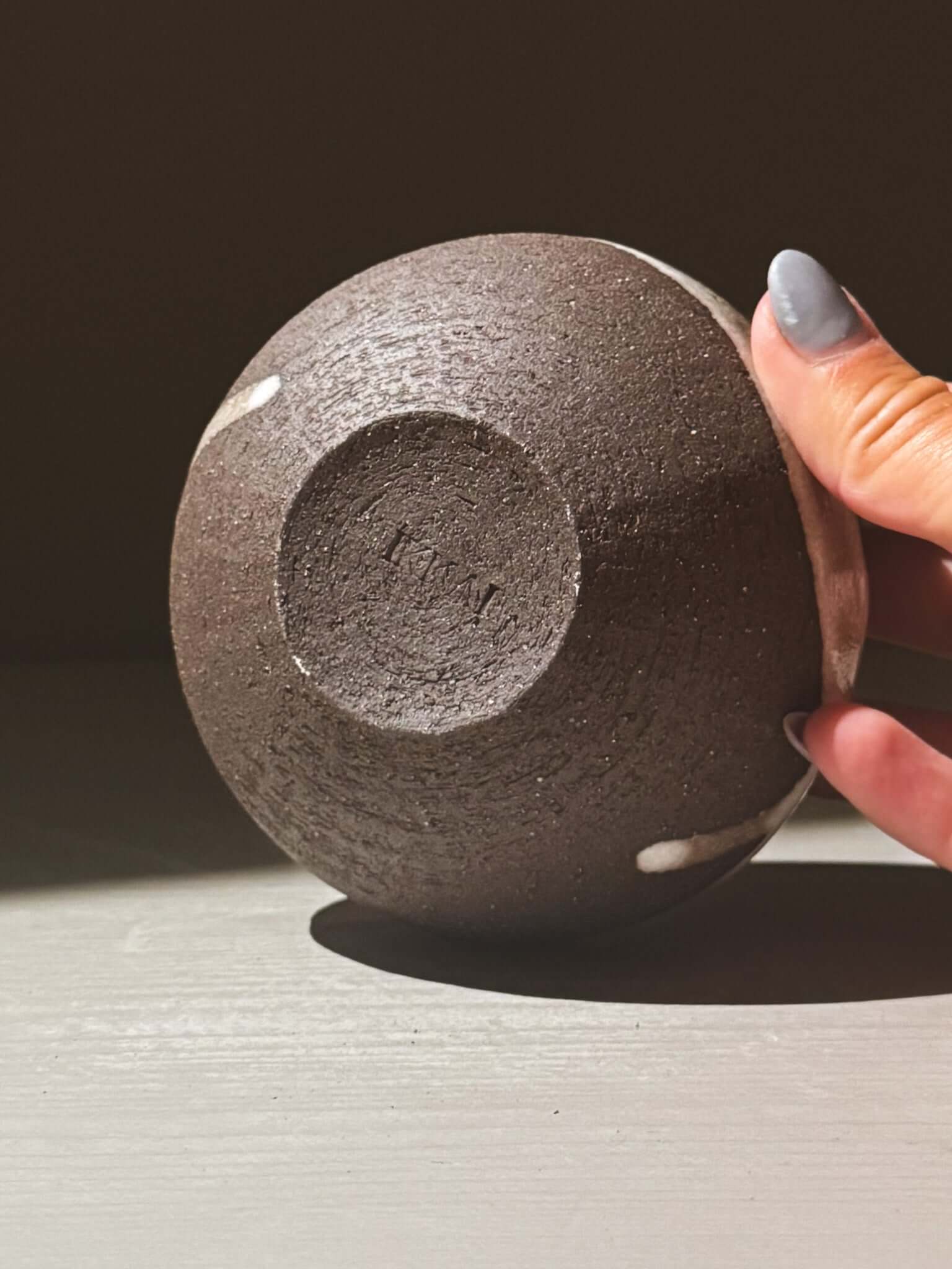 Close-up of hand holding Orb Vase – Yuki Black #11, showing textured clay and unique glaze patterns.